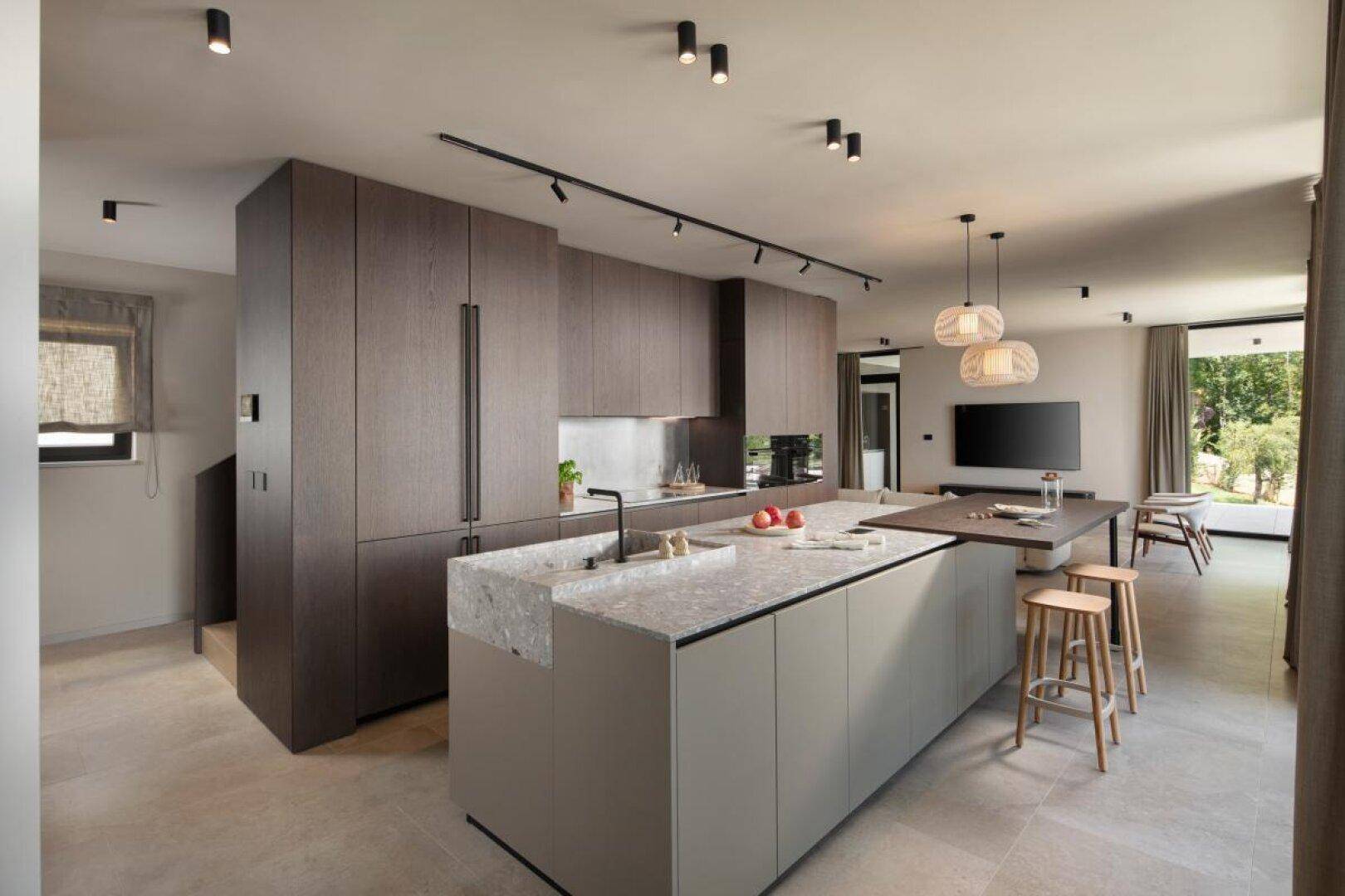 Moderne Küche mit dunklen Holzfronten, Kücheninsel und integrierten Geräten in offenem Wohnbereich.