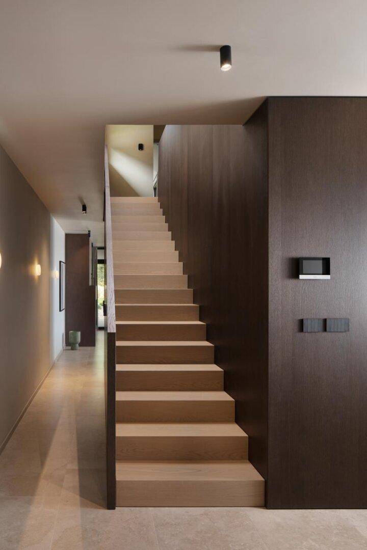 Moderner Flur mit Holztreppe und minimalistischer Beleuchtung, der die verschiedenen Ebenen verbindet.