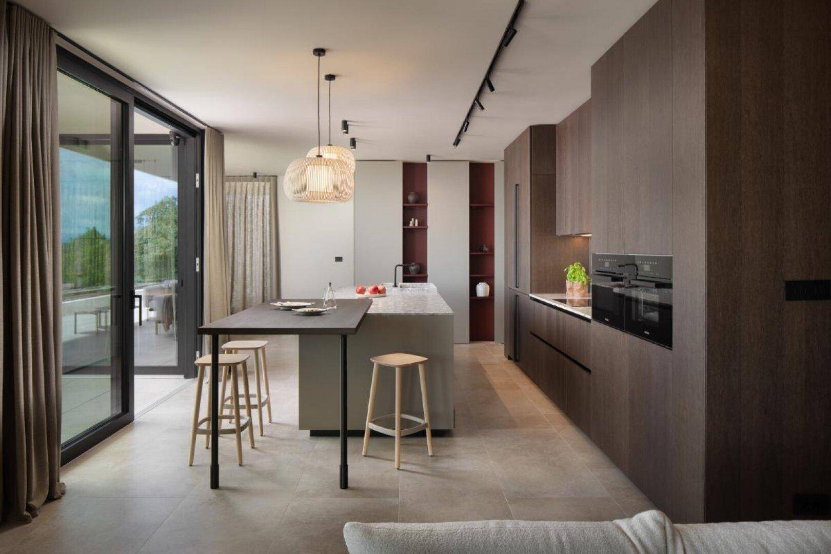 Offene, moderne Küche mit dunklen Schränken, Kücheninsel und Zugang zur Terrasse.