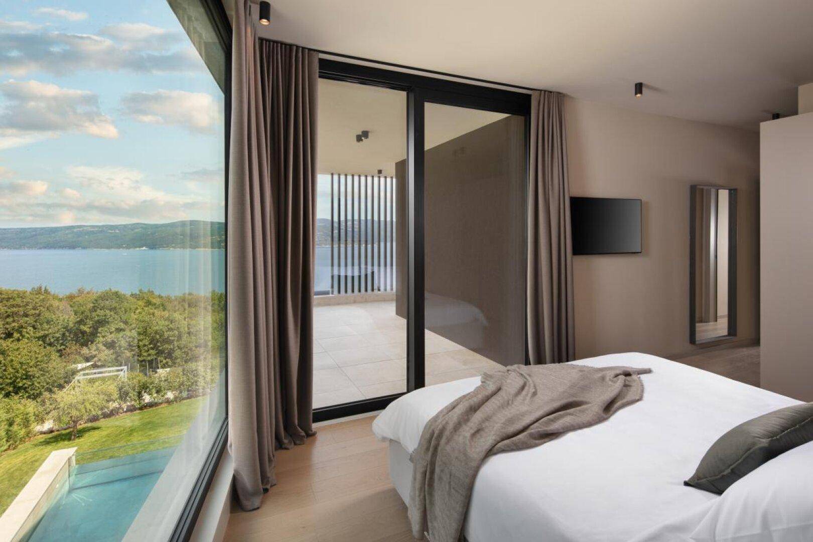 Geräumiges Schlafzimmer mit großen Fenstern, die einen weiten Blick auf das Meer und den Garten bieten.