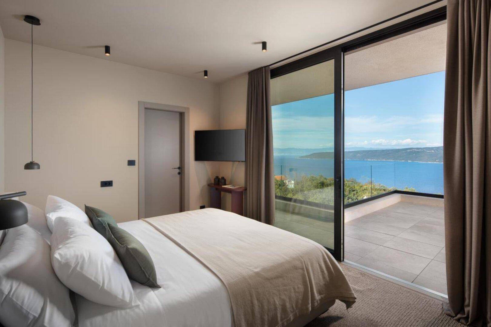 Helles Schlafzimmer mit Doppelbett und direktem Zugang zu einer Terrasse mit Meerblick.