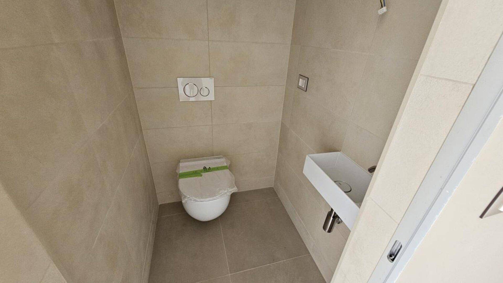 Modernes Gäste-WC mit wandhängender Toilette, kleinem Waschbecken und hellen Fliesen.