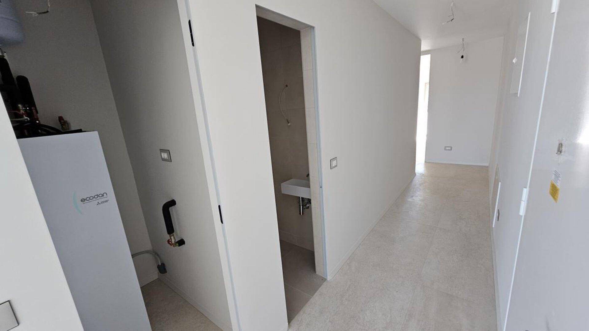 Flur mit Zugang zu einem Gäste-WC und einem Technikraum mit moderner Wärmepumpe.