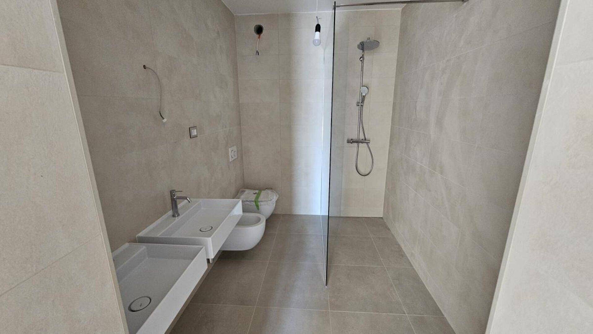 Modernes Badezimmer mit Doppelwaschbecken, wandhängender Toilette und begehbarer Dusche mit Glaswand.