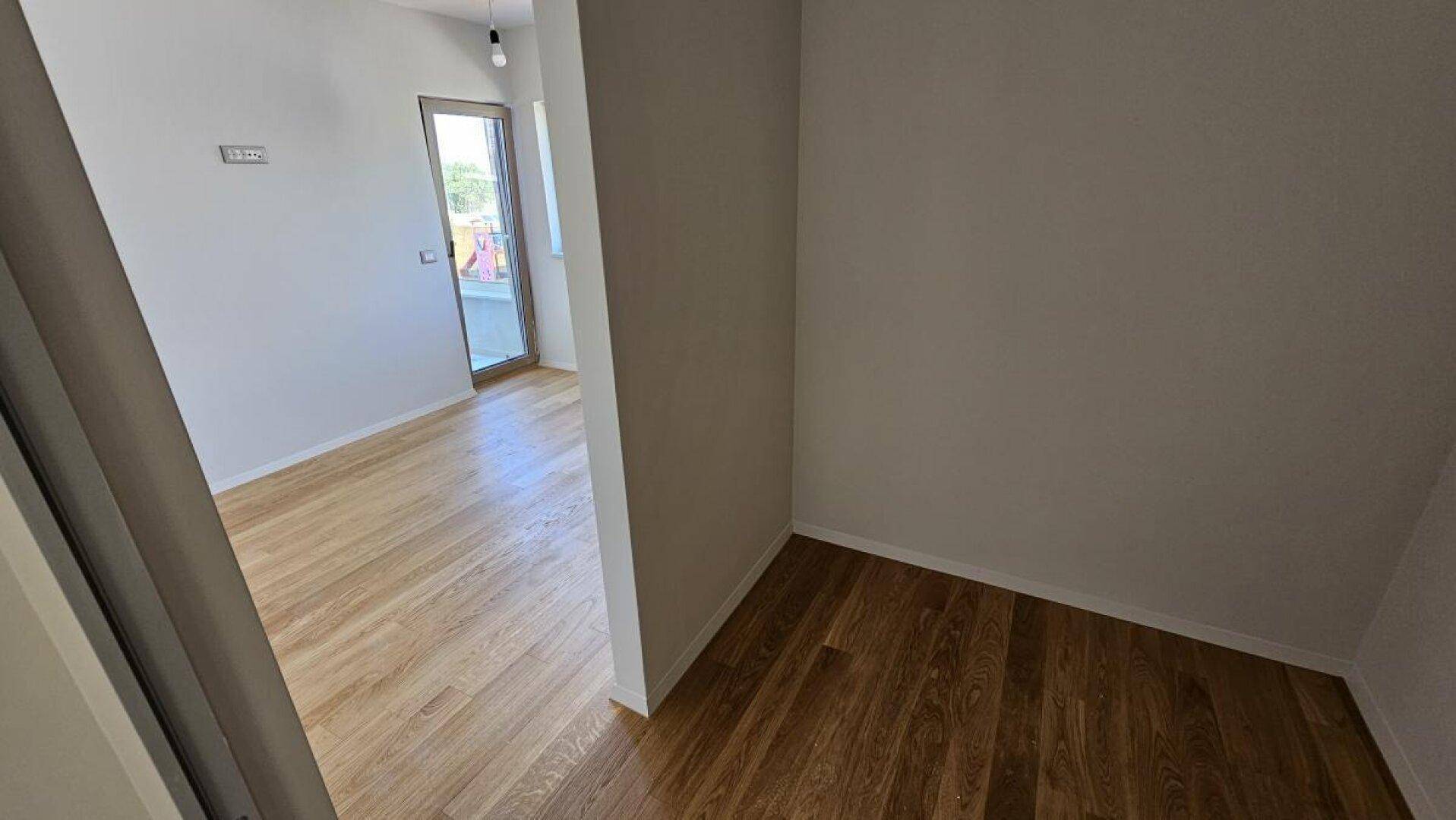 Heller Raum mit Holzdielenboden, gesehen durch eine offene Tür, bereit zur individuellen Einrichtung.