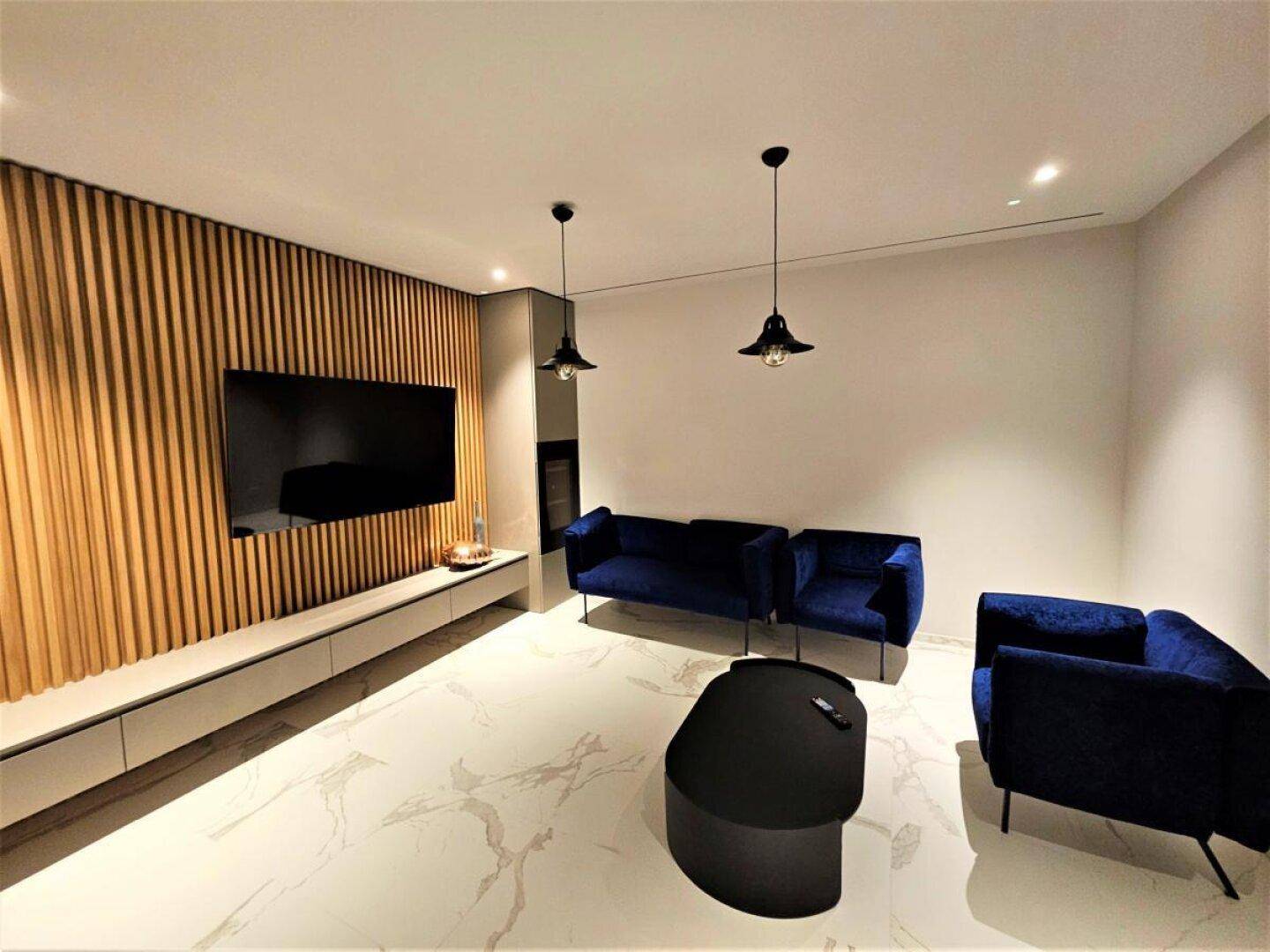 Modernes Wohnzimmer mit dekorativer Holzlamellenwand, Flachbildfernseher und elegantem Marmorfliesenboden.