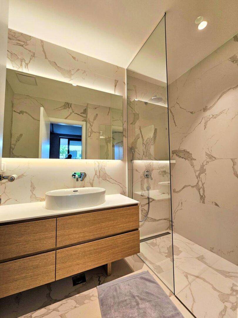 Modernes Badezimmer mit Marmorfliesen, elegantem Waschtisch und großer begehbarer Dusche.