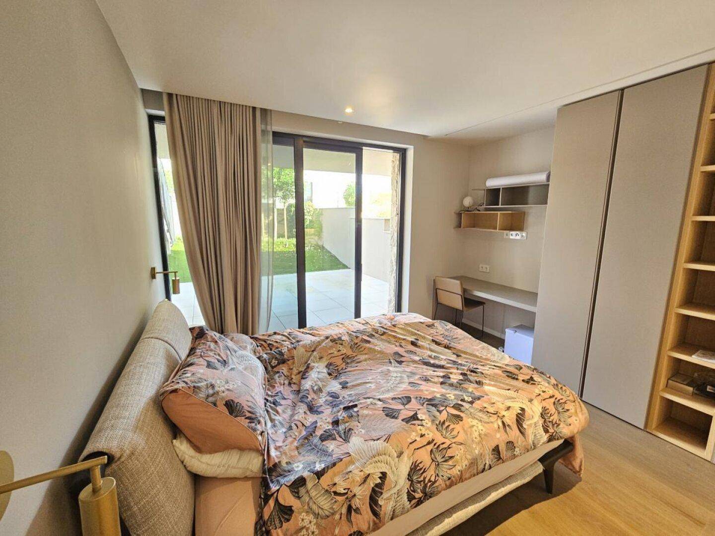 Gemütliches Schlafzimmer mit Schreibtischbereich, Einbauregalen und Zugang zum Garten.