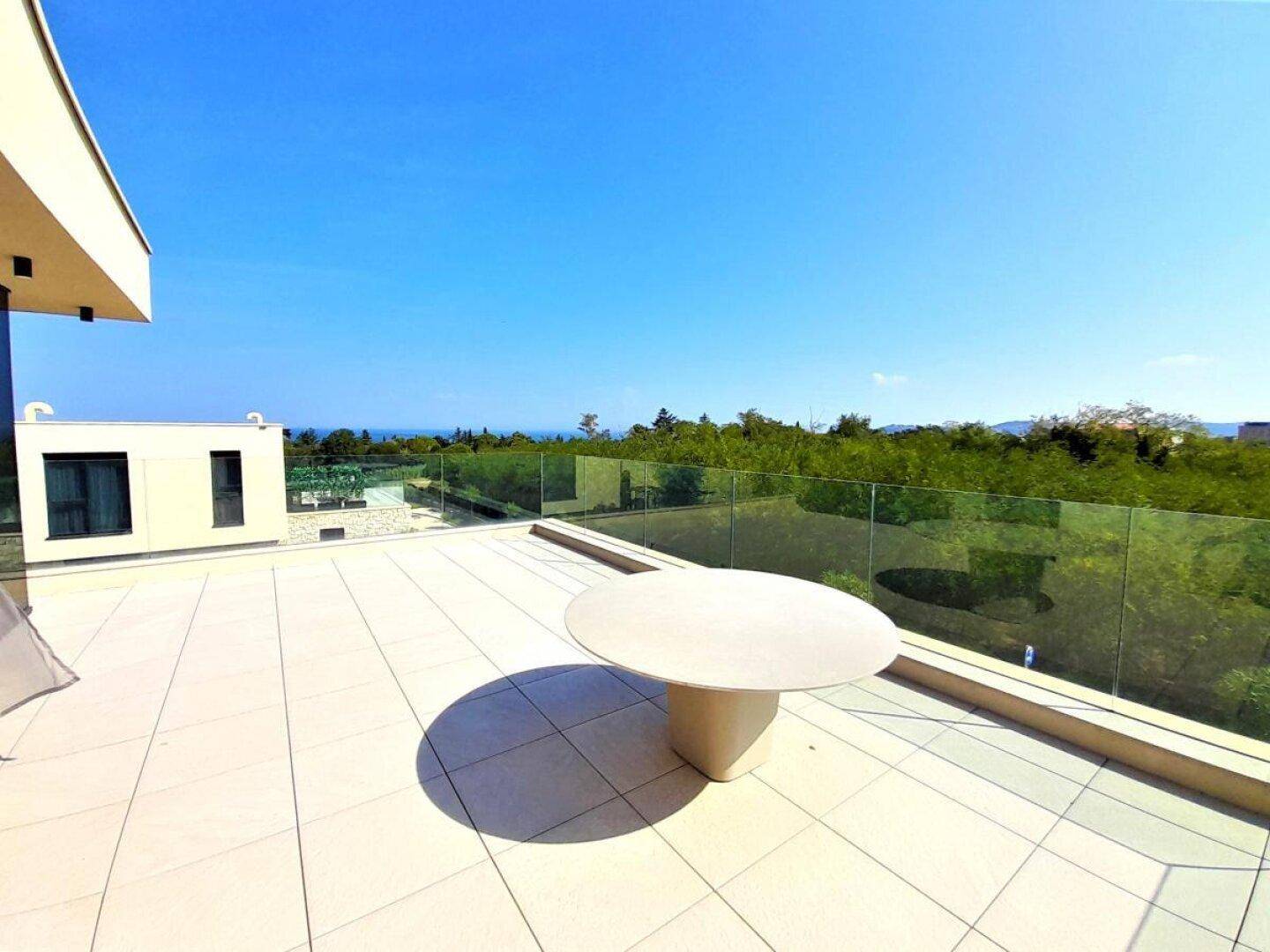 Geräumige Dachterrasse mit einem runden Tisch, umgeben von viel Grün und Meerblick.