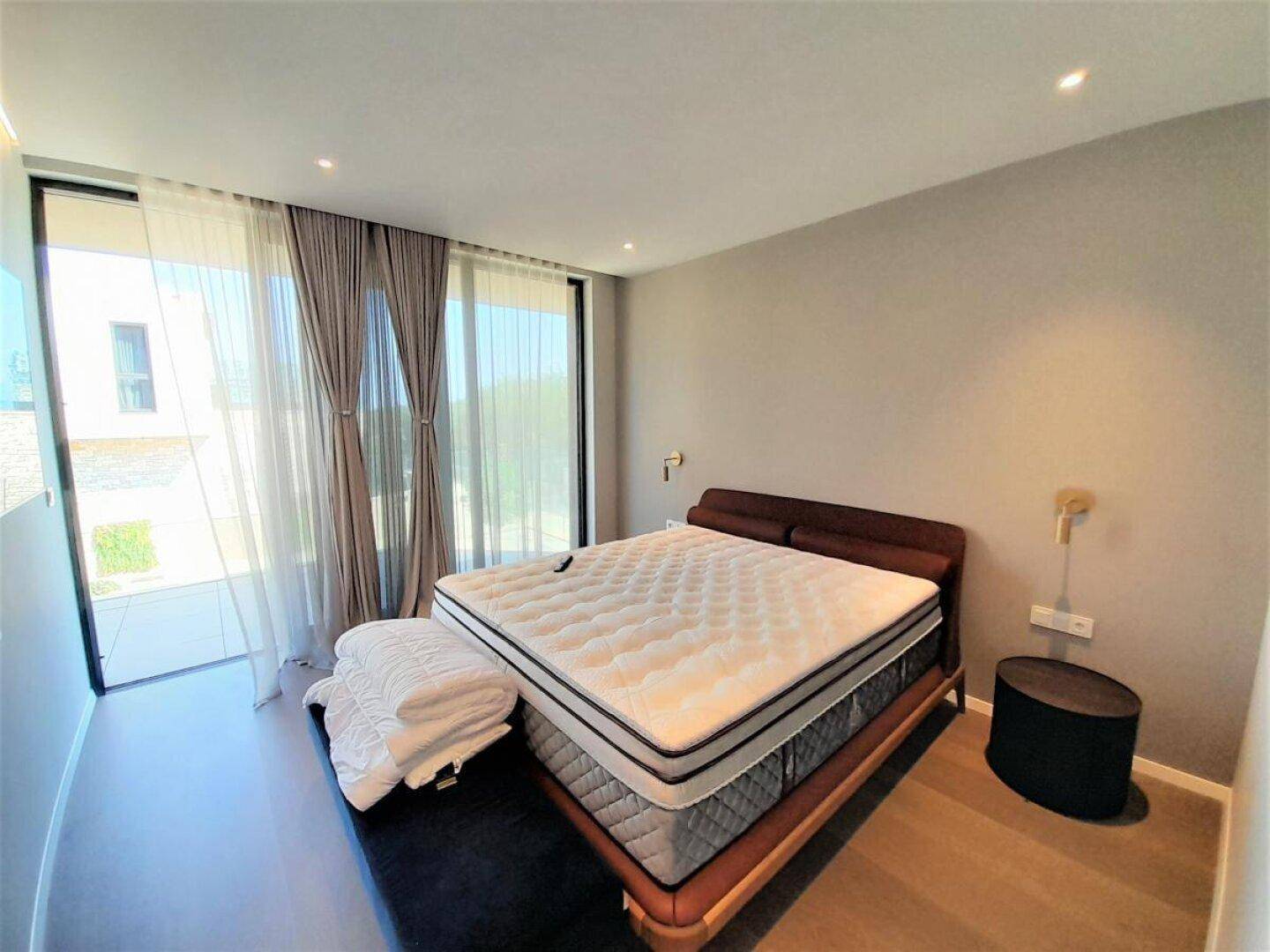 Helles Schlafzimmer mit großem Bett, minimalistischem Design und bodentiefen Fenstern.