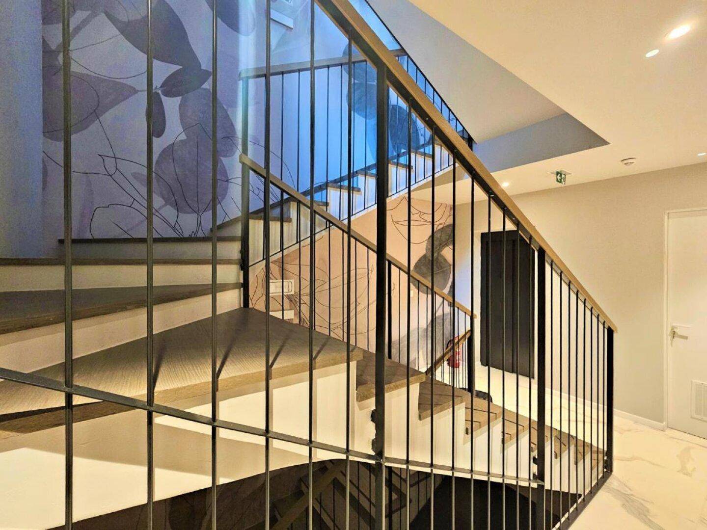 Elegantes Treppenhaus mit modernen Metallgeländern, Holzstufen und dekorativer Wandgestaltung.