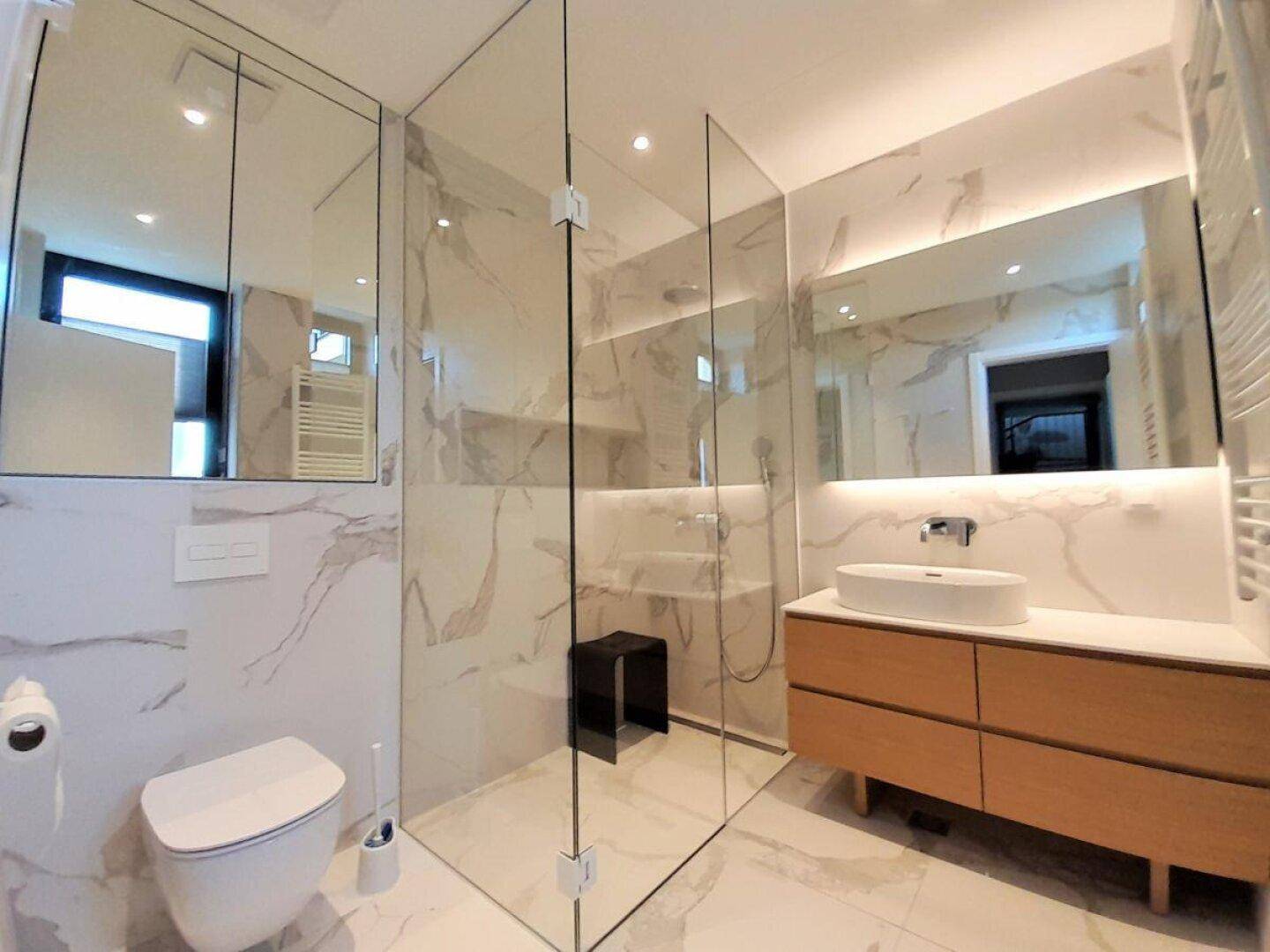 Stilvolles Badezimmer mit Marmoroptik, wandhängendem WC und geräumiger Glasdusche.