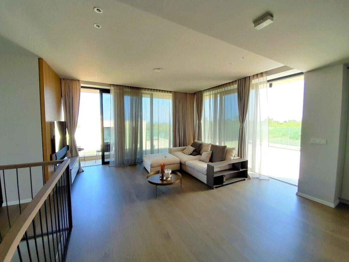 Geräumiges Wohnzimmer mit bequemer Couch, dekorativer Holzwand und bodentiefen Fenstern.