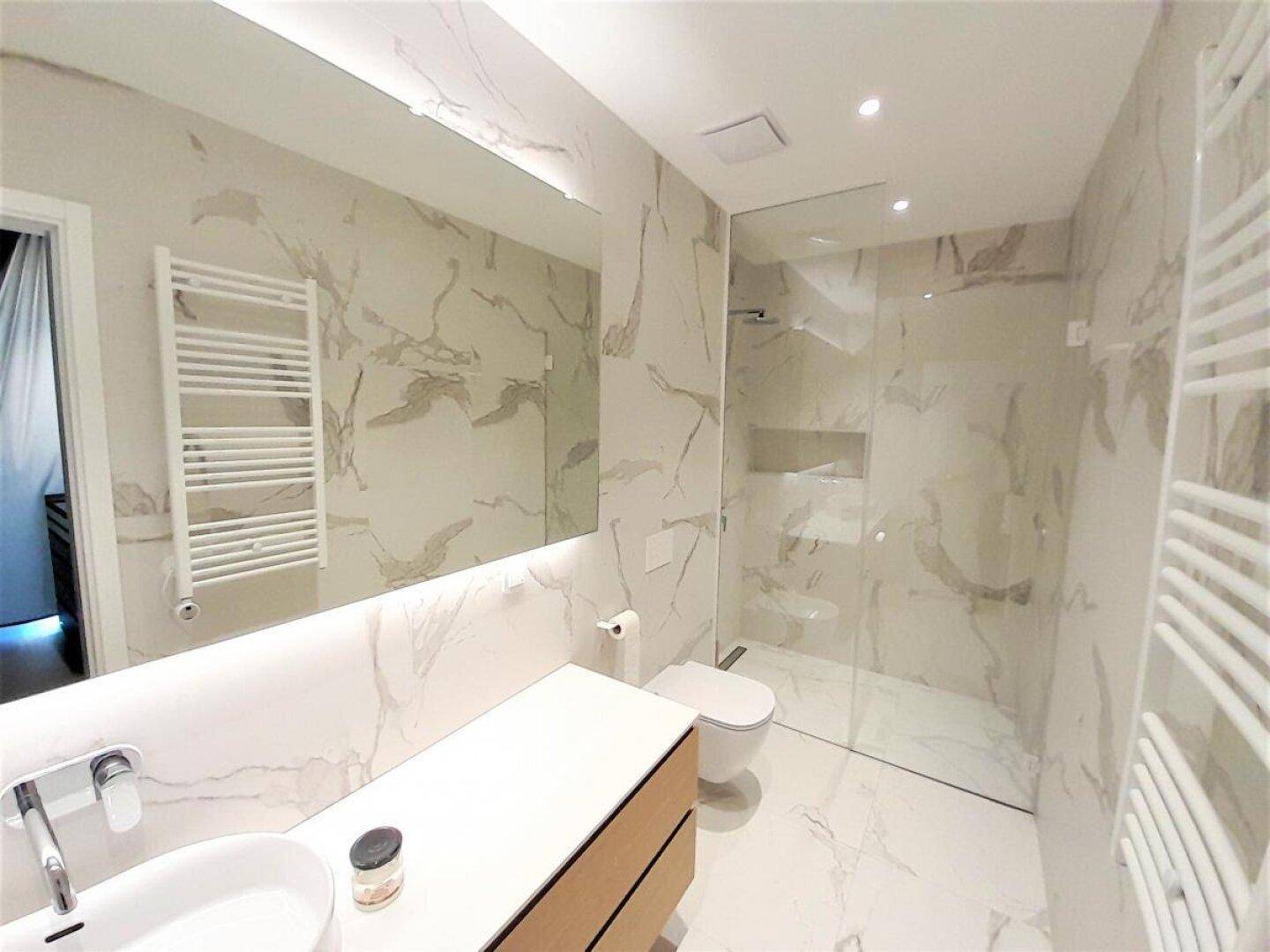 Elegantes Badezimmer mit Marmorfliesen, modernem Waschtisch und geräumiger begehbarer Dusche.