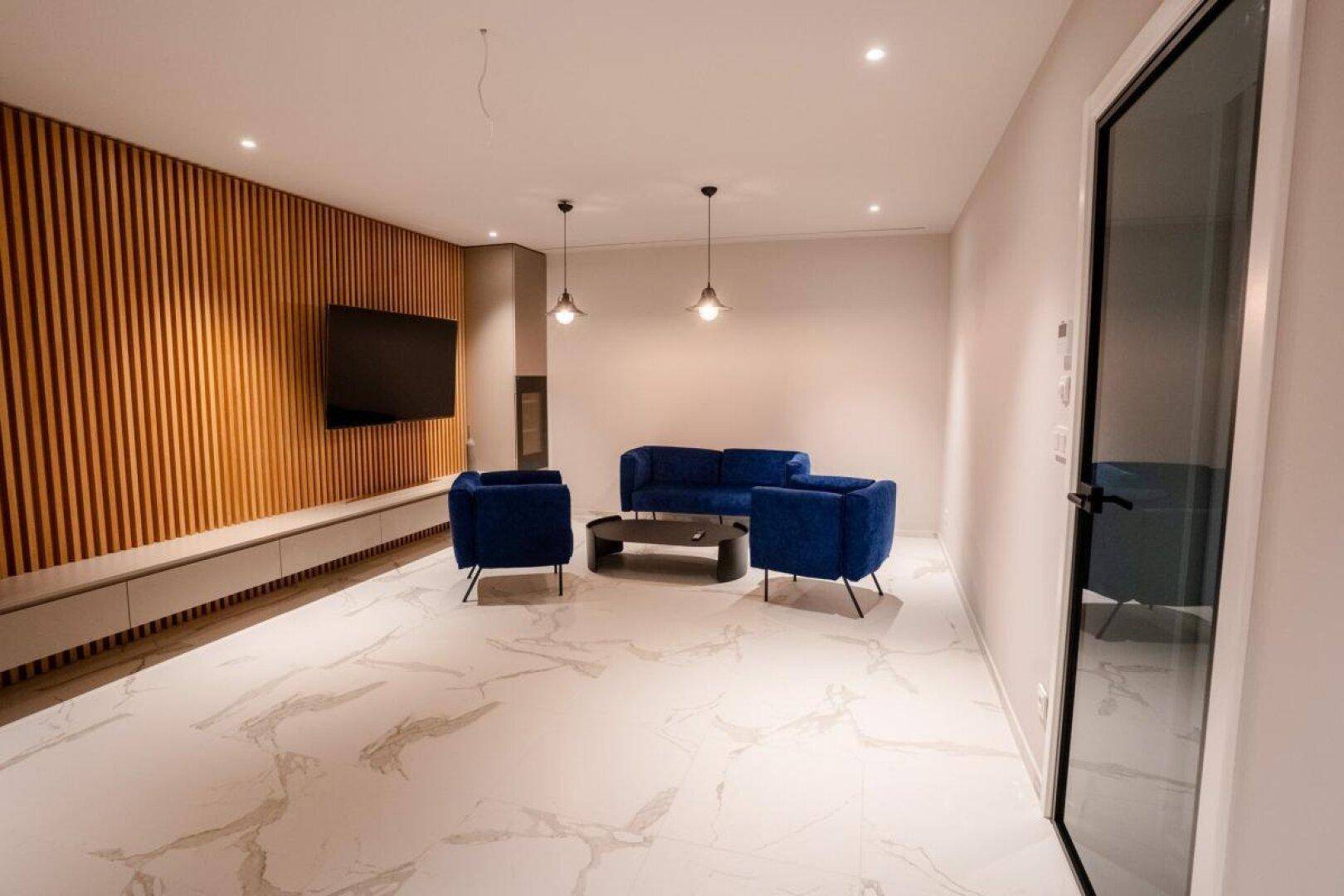Stilvolles Wohnzimmer mit blauen Sofas, Holzlamellenwand und glänzendem Marmorfliesenboden.