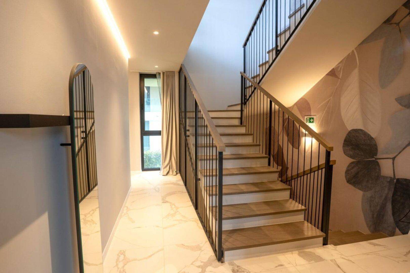 Heller Flur mit moderner Treppe, großem Spiegel und stilvoller Wandtapete.