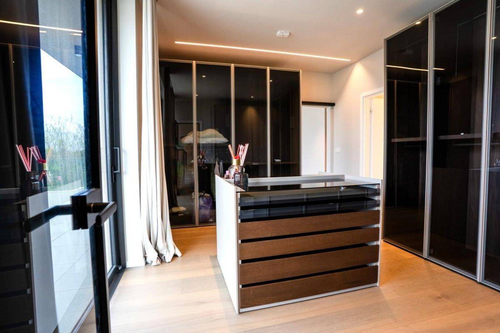 Luxuriöser begehbarer Kleiderschrank mit zentraler Insel, viel Stauraum und großen Fenstern.
