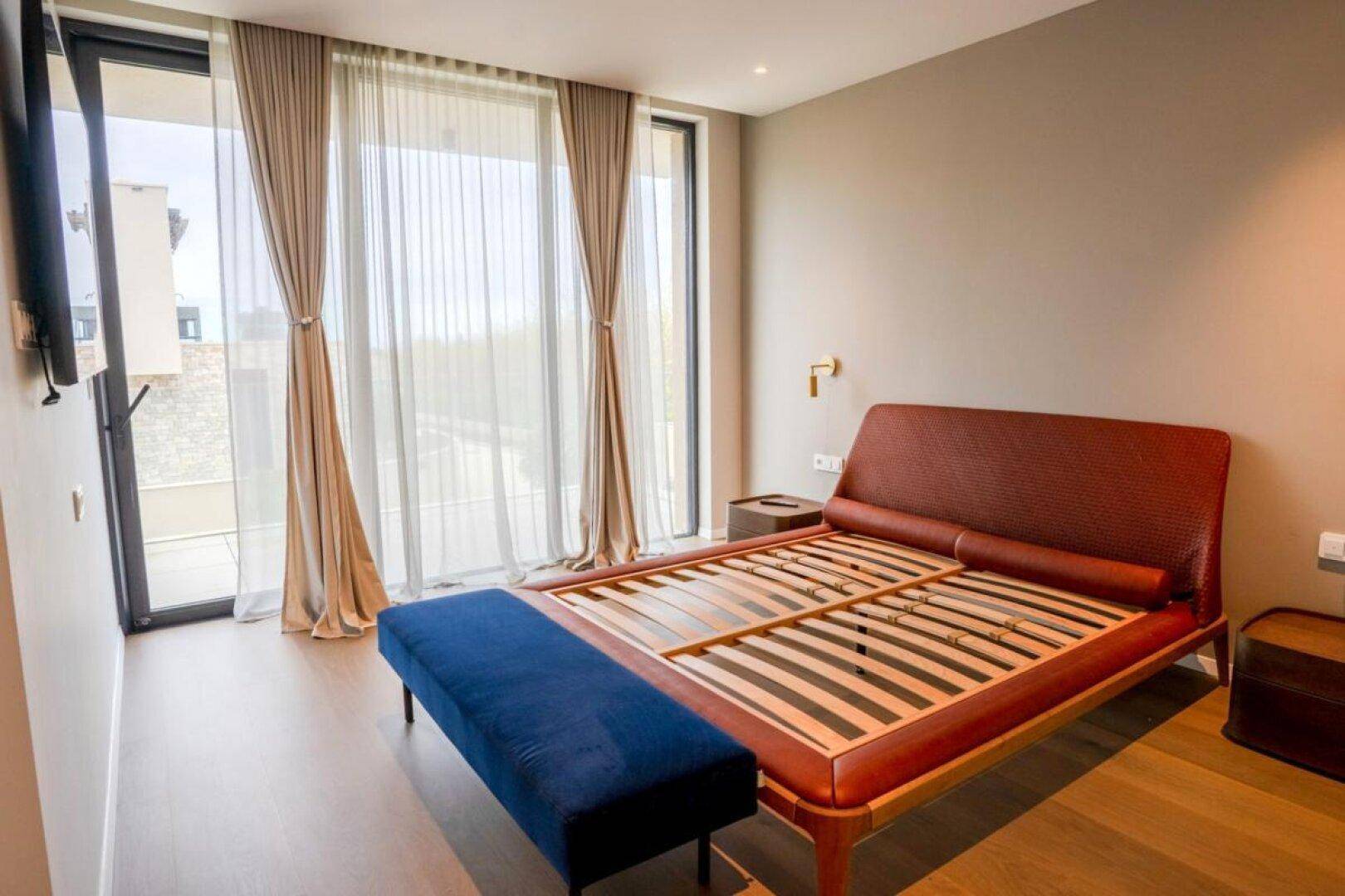 Helles Schlafzimmer mit modernem Bettrahmen, blauer Sitzbank und bodentiefen Fenstern.
