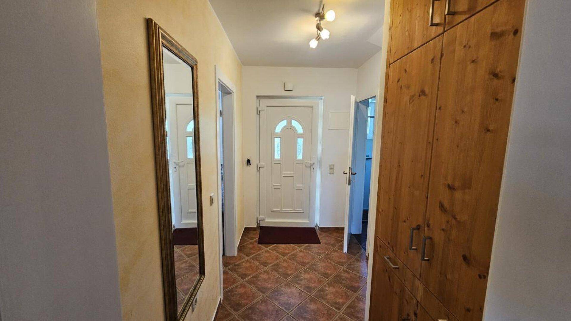Heller Eingangsbereich mit Fliesenboden, großem Spiegel und praktischem Einbauschrank aus Holz.