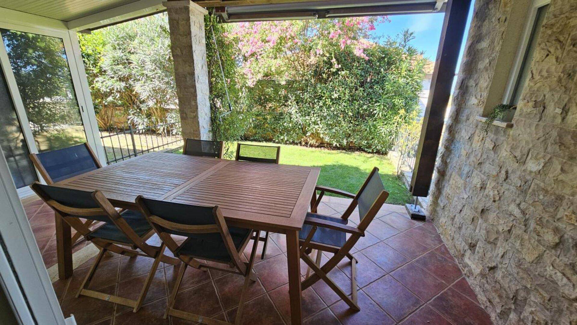 Überdachte Terrasse mit großem Holztisch und Gartenblick, ideal für entspannte Stunden im Freien.