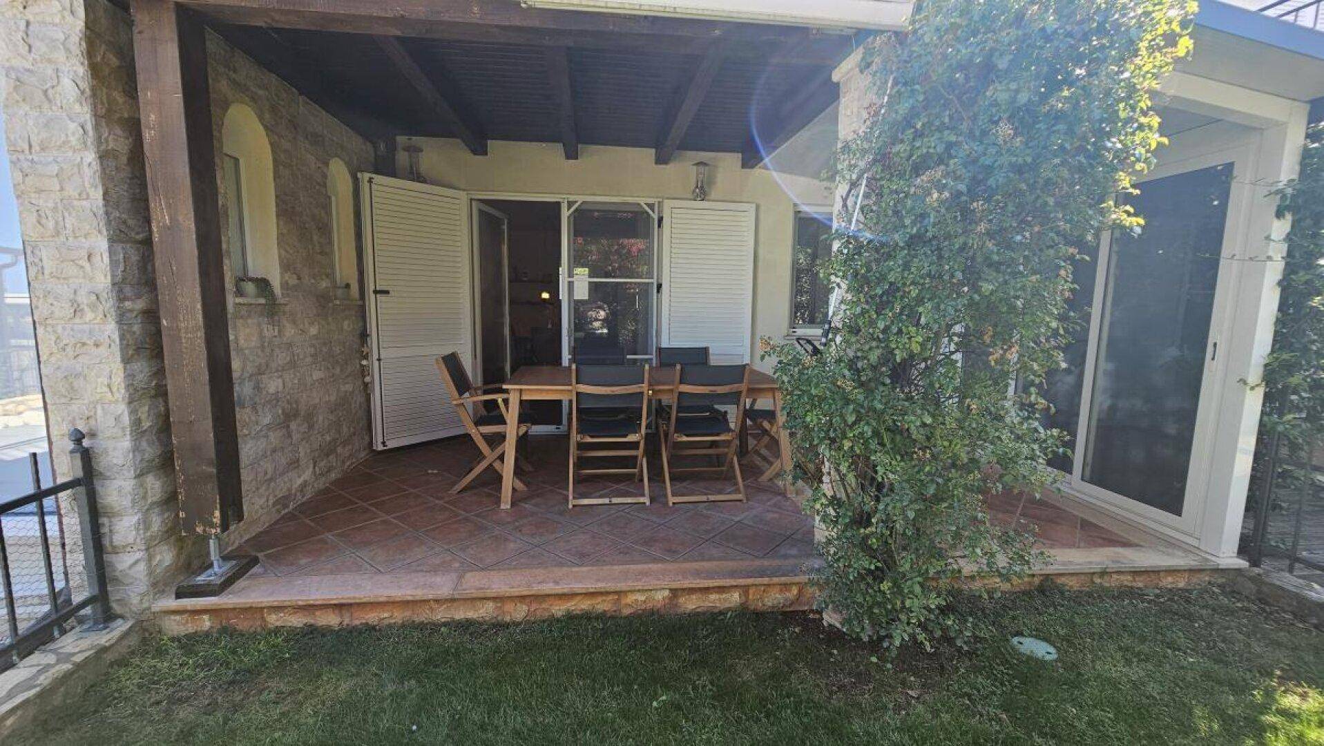 Geräumige überdachte Terrasse mit Steinfassade und Zugang zum gepflegten Rasenbereich.