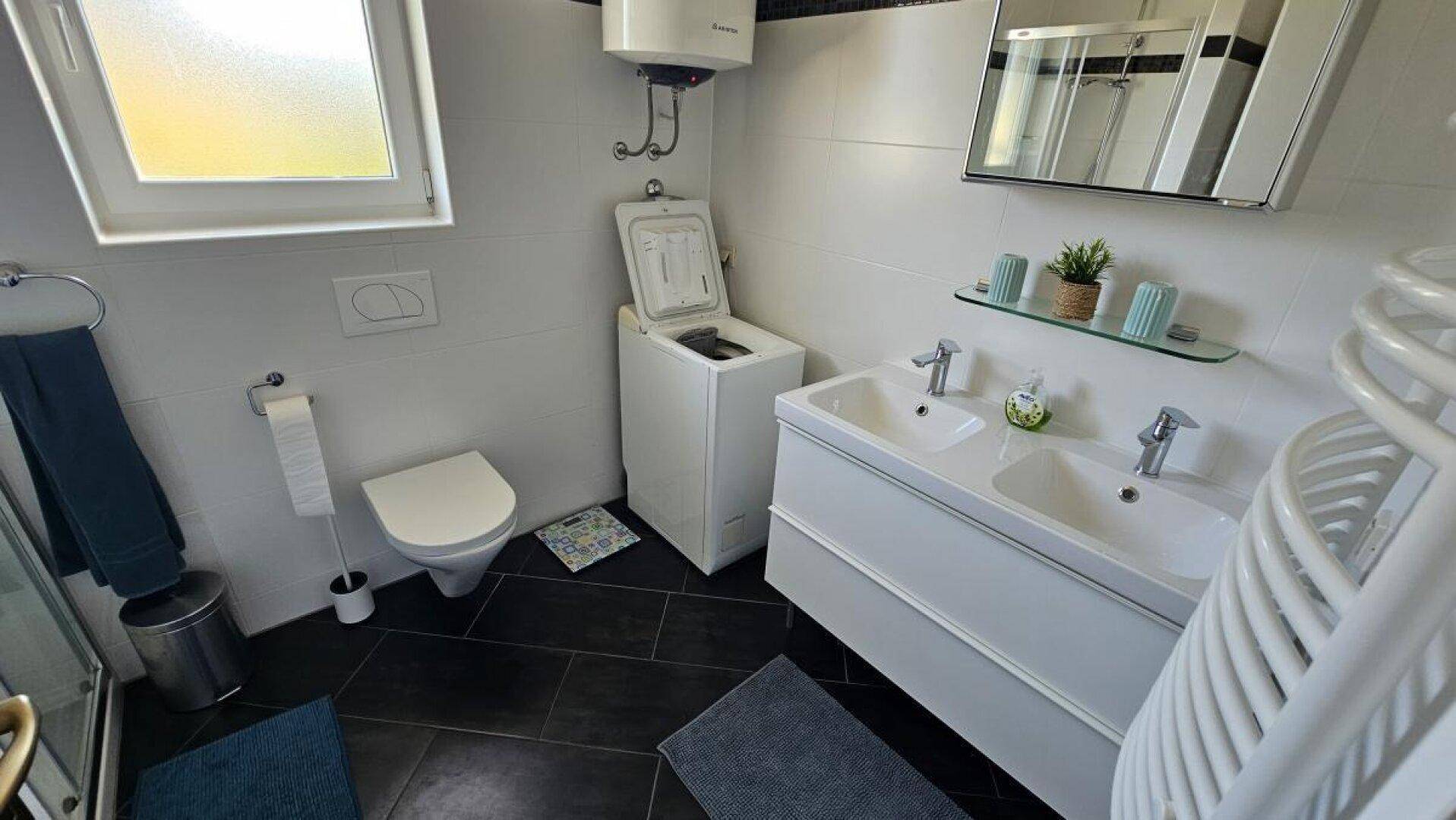 Modernes Badezimmer mit Doppelwaschbecken, Dusche, WC und Waschmaschine, ausgestattet mit Fenster.