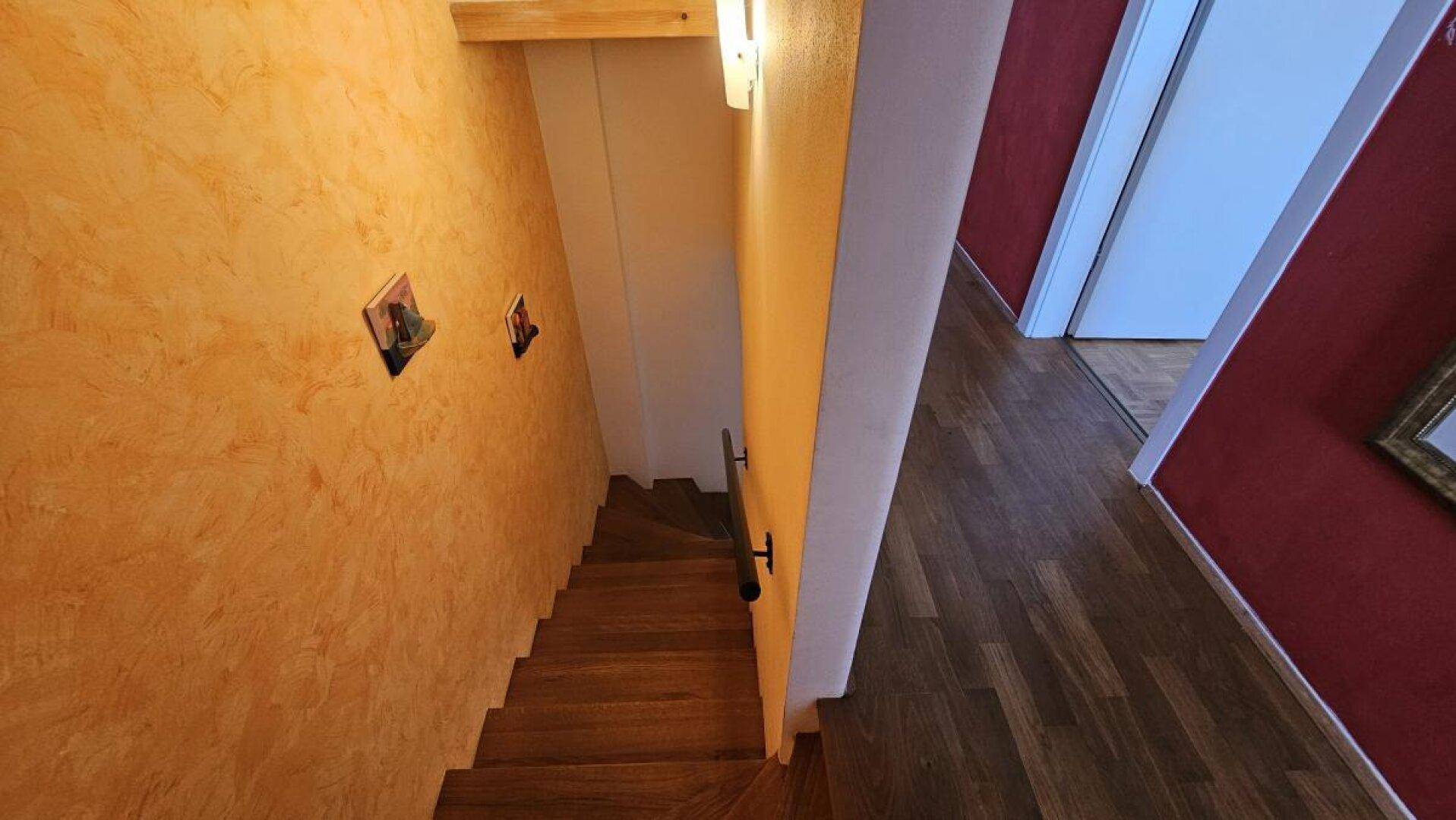 Holztreppe mit einer auffälligen orangefarbenen Wandgestaltung, die zu den oberen Etagen führt.