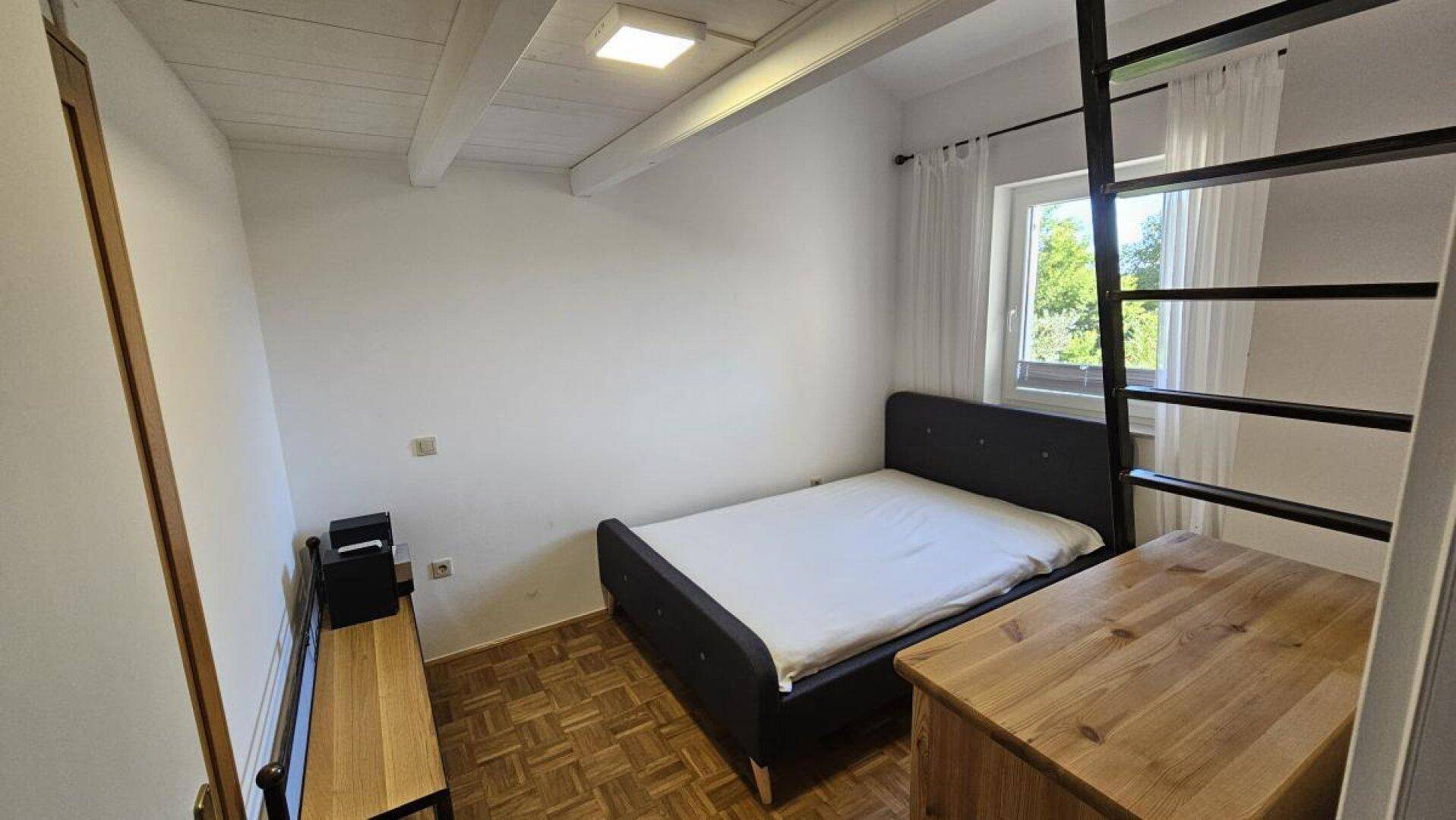 Schlafzimmer mit Doppelbett, Holzkommode und Leiter zum Hochbett, unter sichtbaren Deckenbalken.
