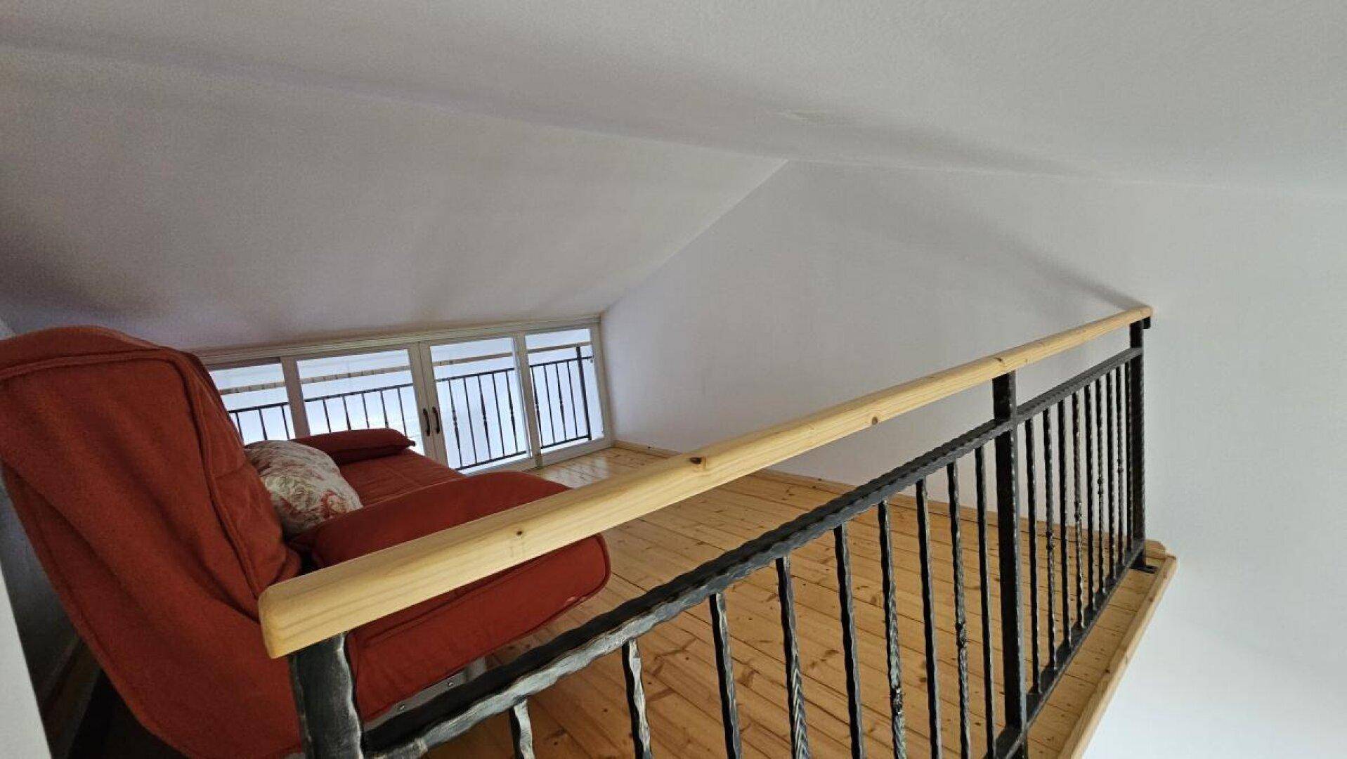 Gemütlicher Loftbereich mit rotem Sofa und Geländer, der zusätzlichen Wohnraum bietet.