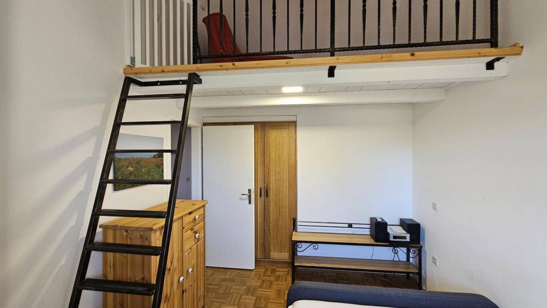 Schlafzimmer mit Leiter zum Hochbett, Holzkommode und Kleiderschrank, auf Parkettboden.