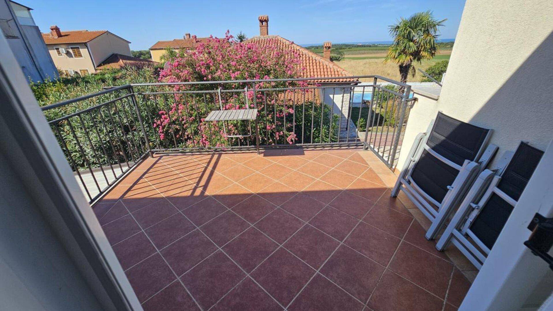 Sonniger Balkon mit Fliesenboden, Liegestühlen und weitem Blick über Felder bis zum Meer.