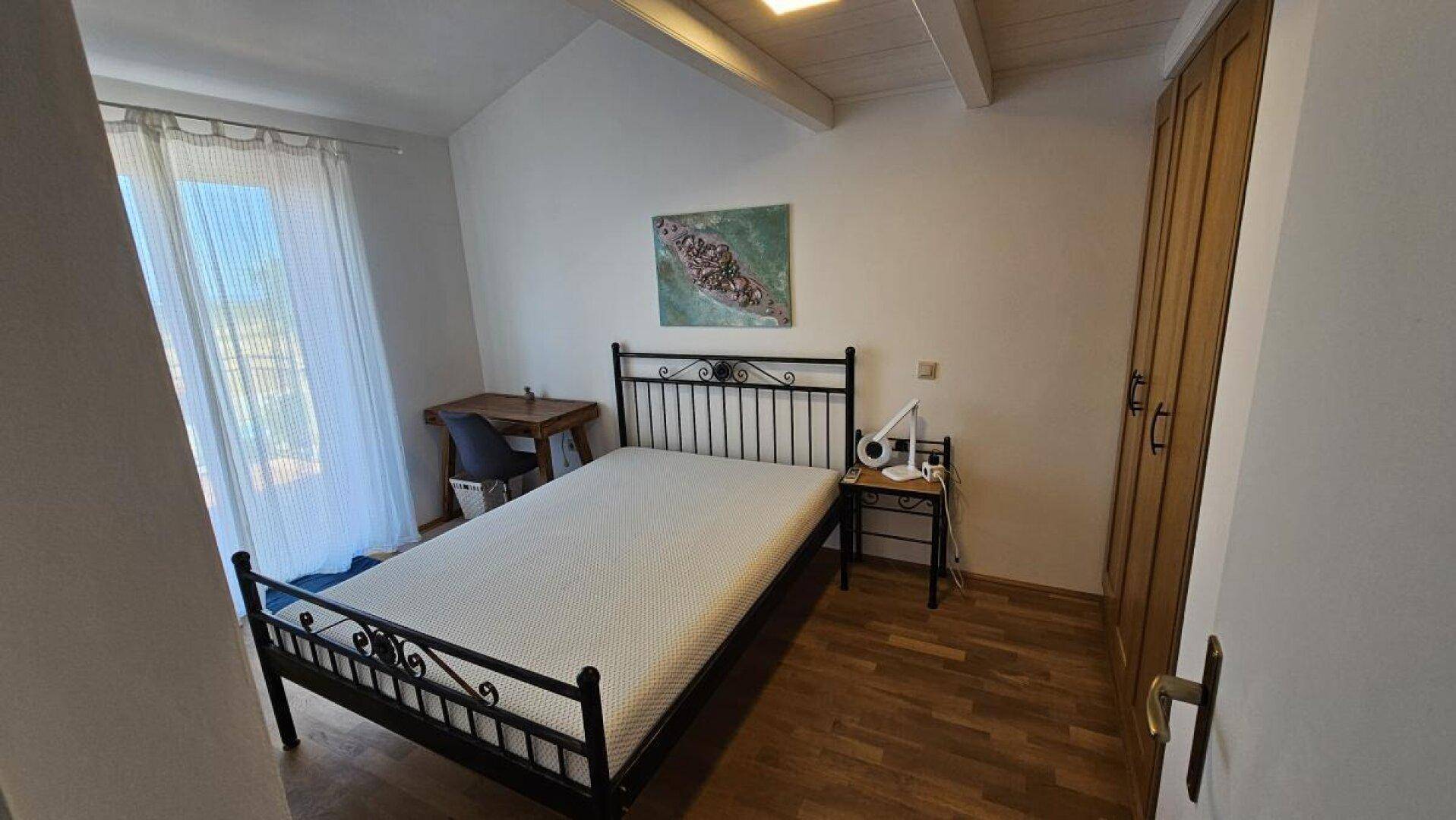 Schlafzimmer mit Doppelbett, Schreibtisch und Kleiderschrank, mit Zugang zu einem französischen Balkon.