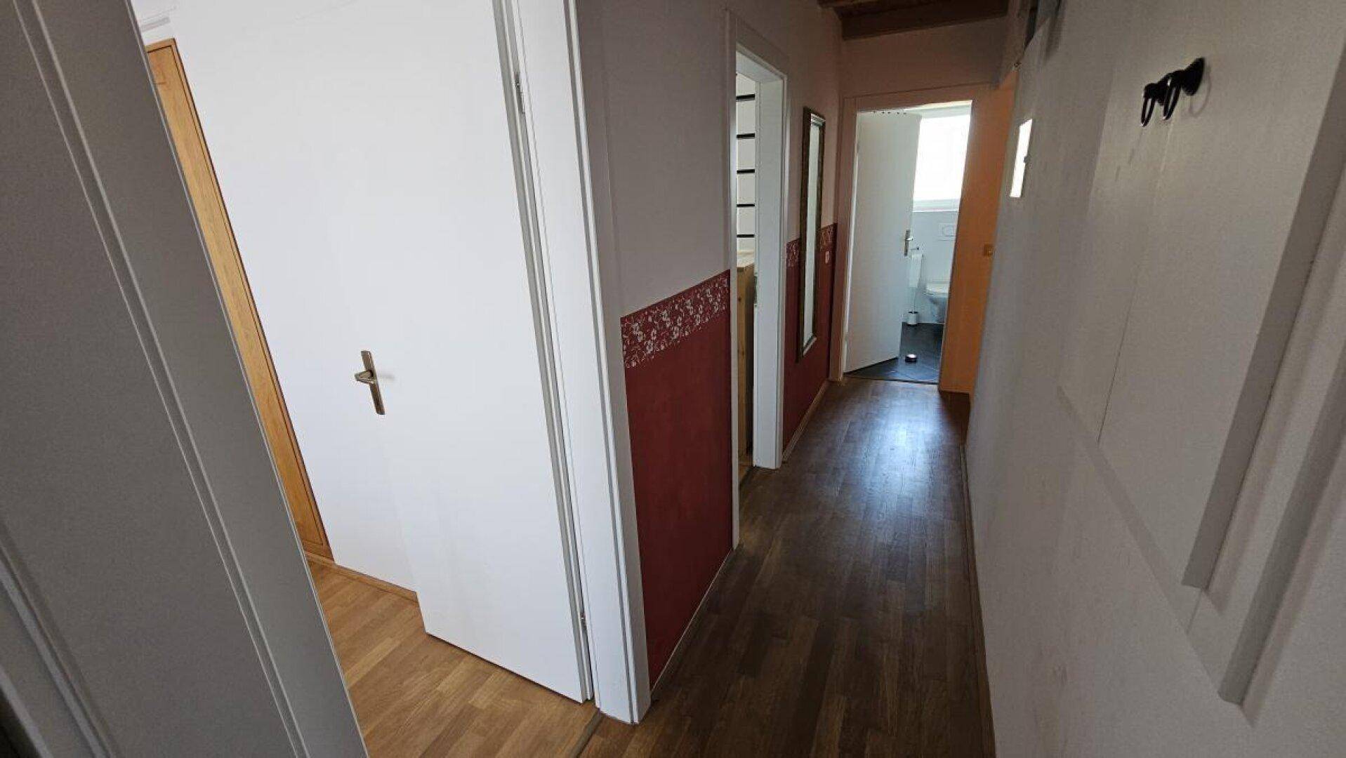 Langer Flur mit Holzboden und roten Akzentwänden, der zu verschiedenen Räumen führt.