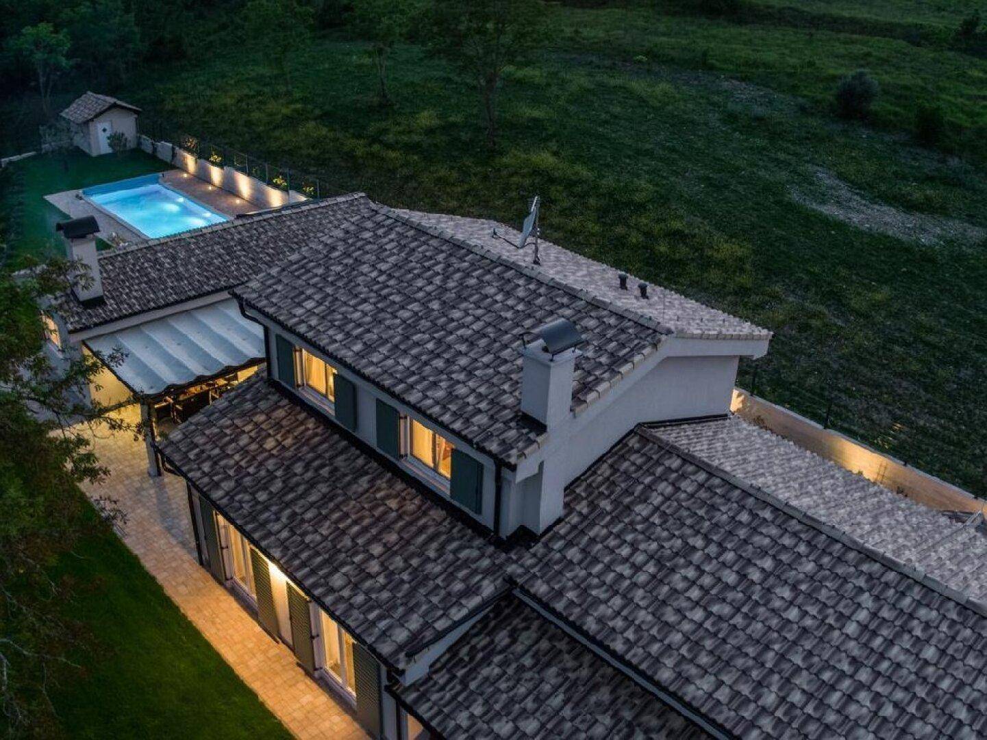 Detaillierte Nachtansicht des Daches einer Villa mit traditionellen Ziegeln und beleuchteten Fenstern.