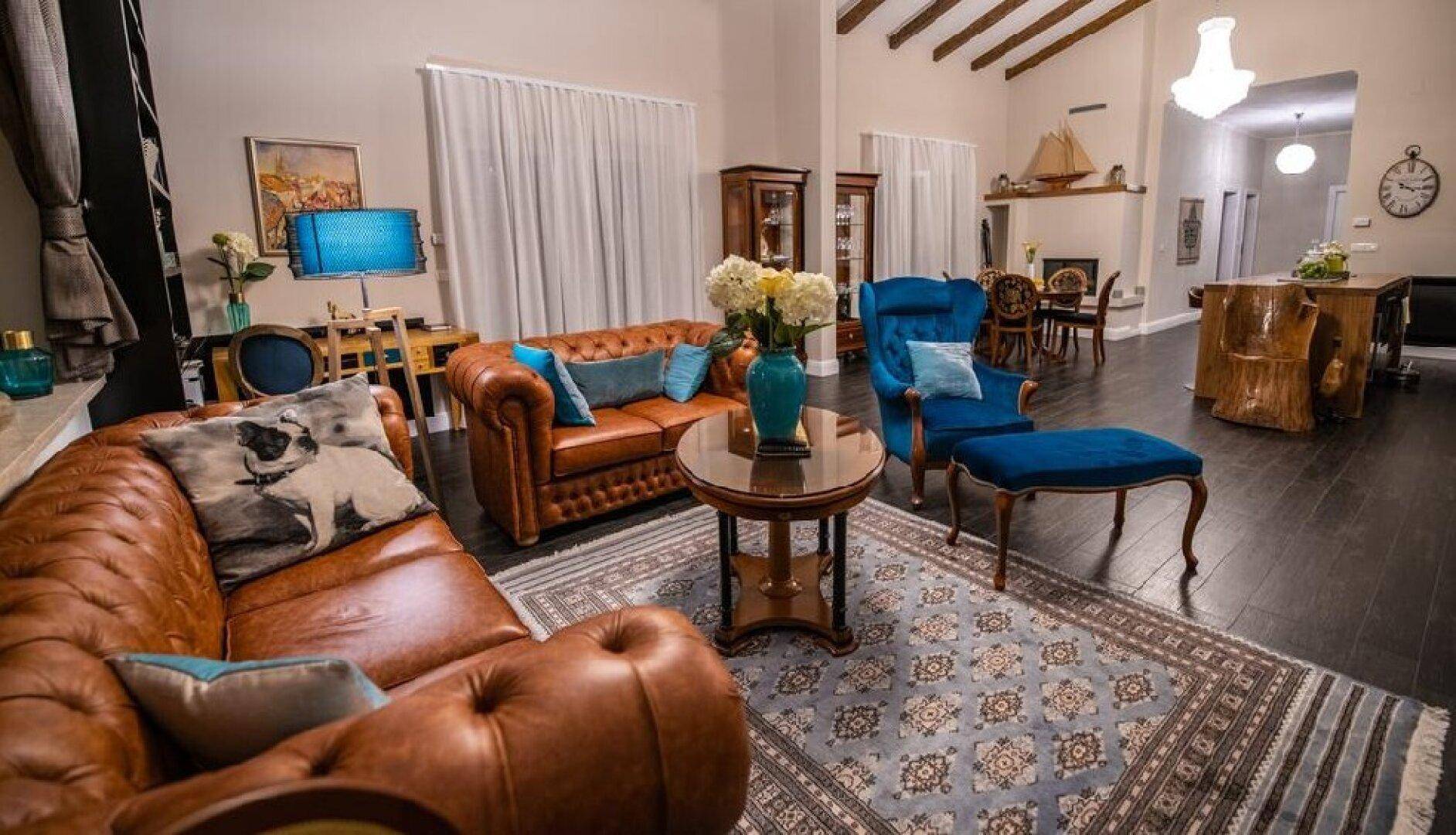 Geräumiges Wohnzimmer mit Ledersofas, Teppich, Holzbalken und einem Kronleuchter, offen zum Essbereich.