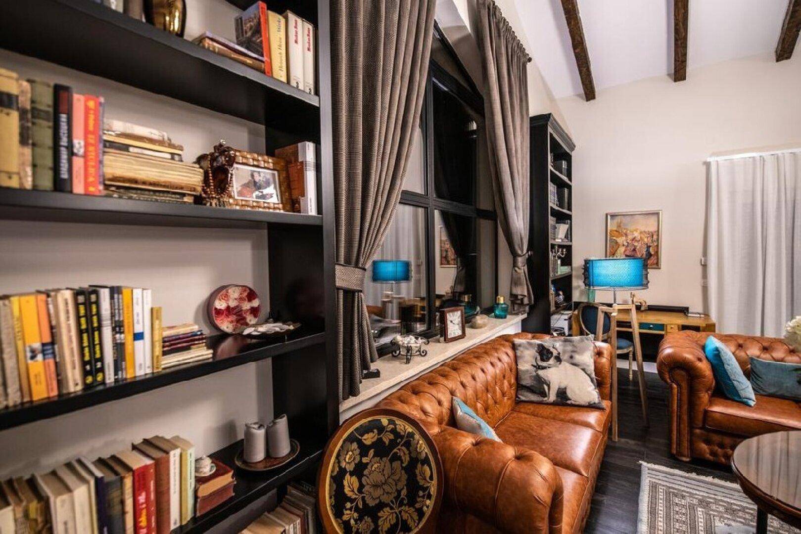 Elegantes Wohnzimmer mit Ledersofas, Bücherregalen und großen Fenstern, die viel Licht hereinlassen.
