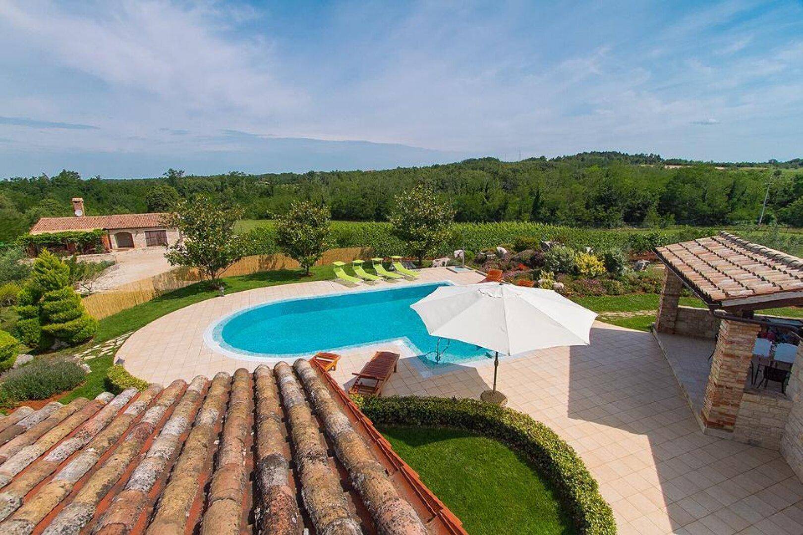 Panoramablick auf die weitläufige Poolanlage mit Sonnenliegen und die umliegende grüne Landschaft mit Weinbergen.