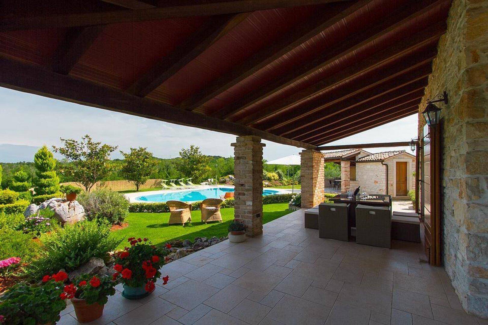 Überdachte Terrasse mit Essbereich und Lounge-Möbeln, bietet einen schönen Blick auf den Pool und die Landschaft.