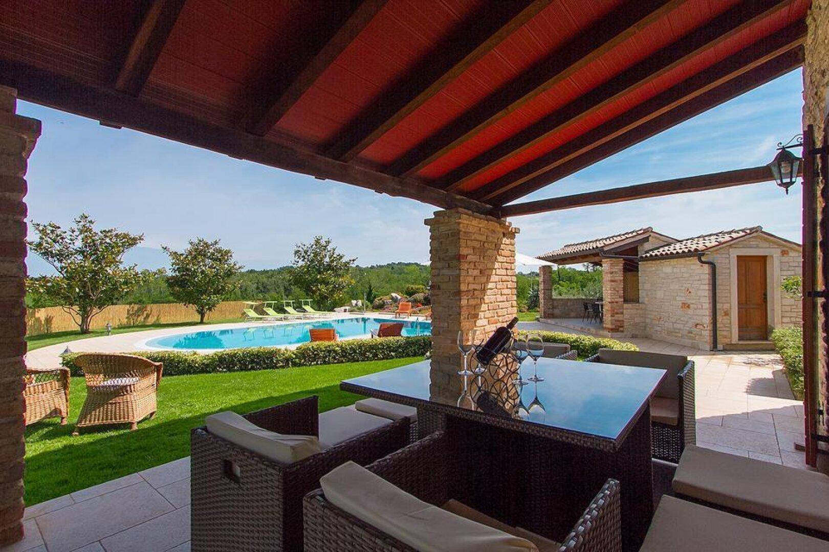 Stilvolle überdachte Terrasse mit Lounge-Möbeln und Blick auf den Pool und den gepflegten Gartenbereich.