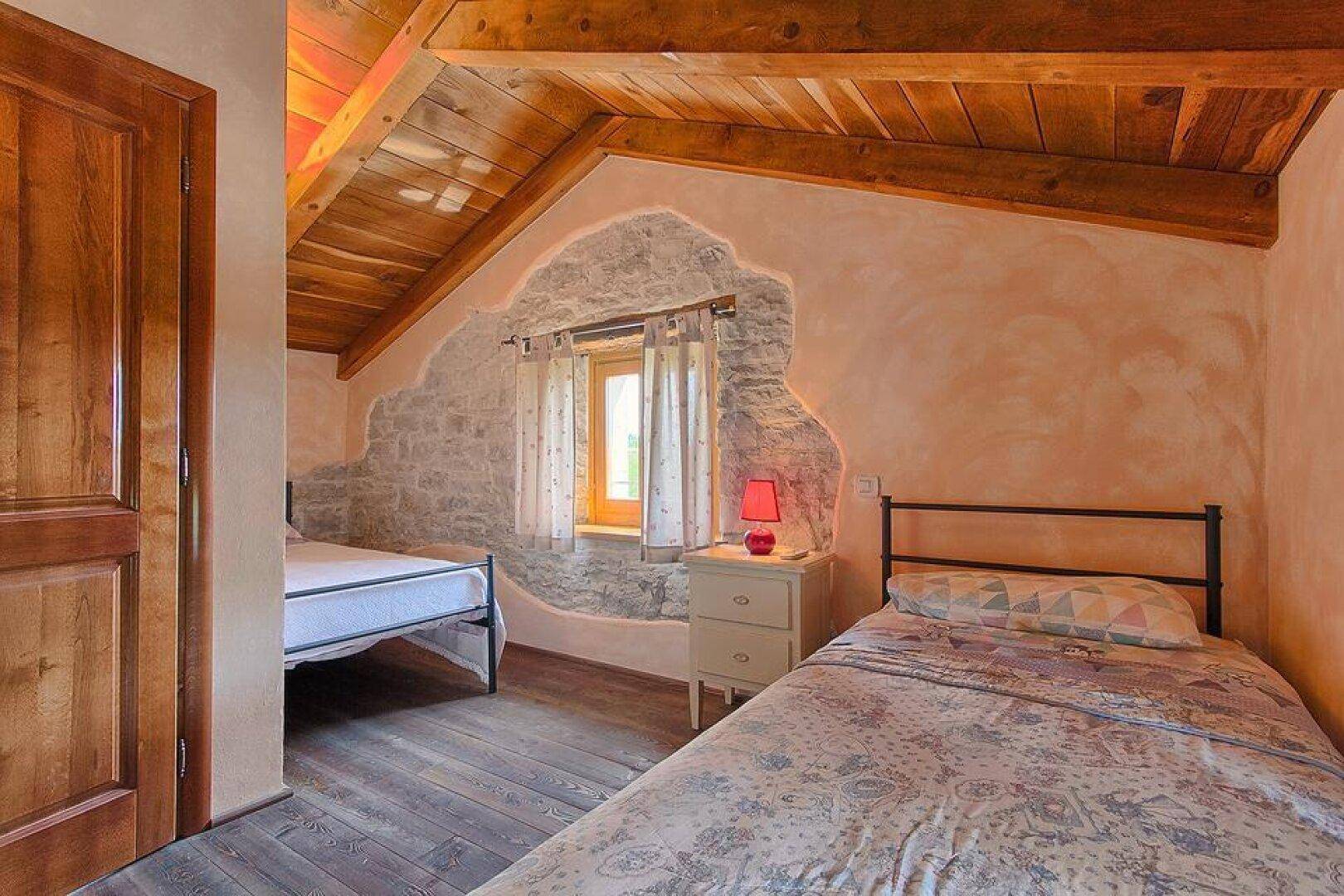 Rustikales Schlafzimmer im Dachgeschoss mit Holzbalkendecke, freigelegten Steinwänden und zwei Einzelbetten.