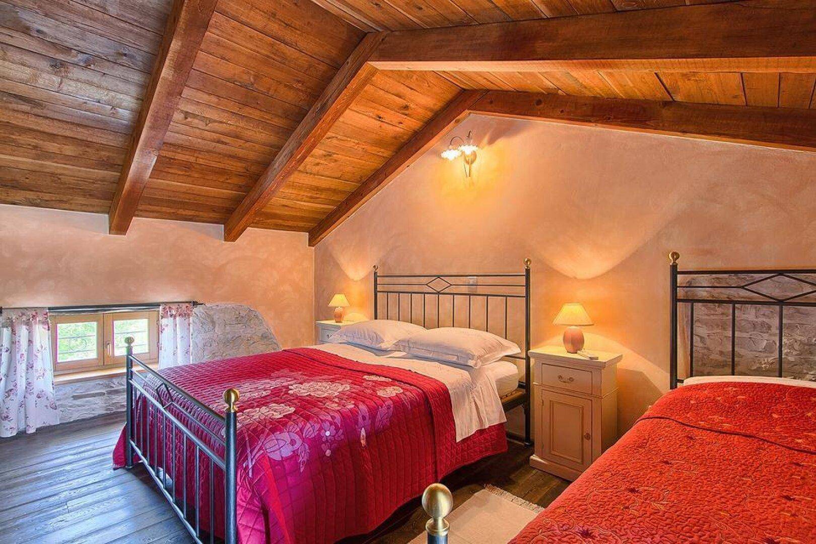 Gemütliches Schlafzimmer im Dachgeschoss mit Holzbalkendecke, Doppelbett und Einzelbett, ideal für Familien.