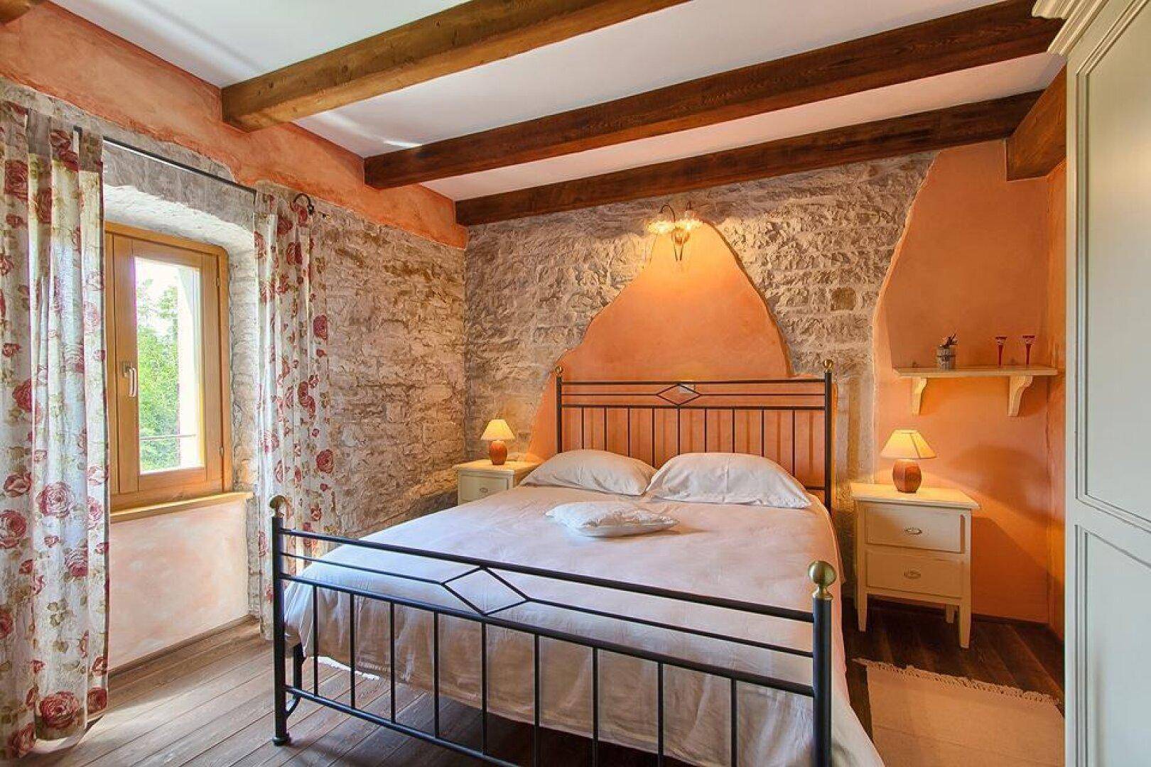 Charmantes Schlafzimmer mit freigelegten Steinwänden, Holzbalken und einem schmiedeeisernen Doppelbett.