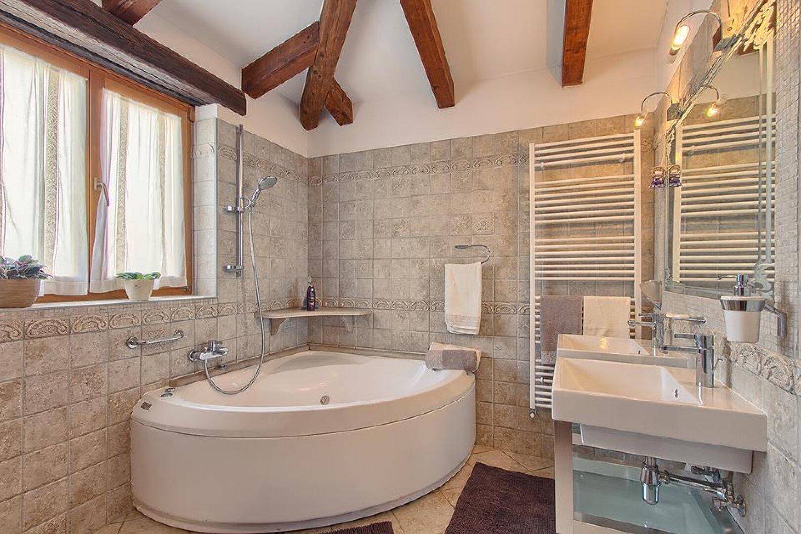 Geräumiges Badezimmer mit Eckbadewanne, modernem Waschbecken, beheiztem Handtuchhalter und Fenster.