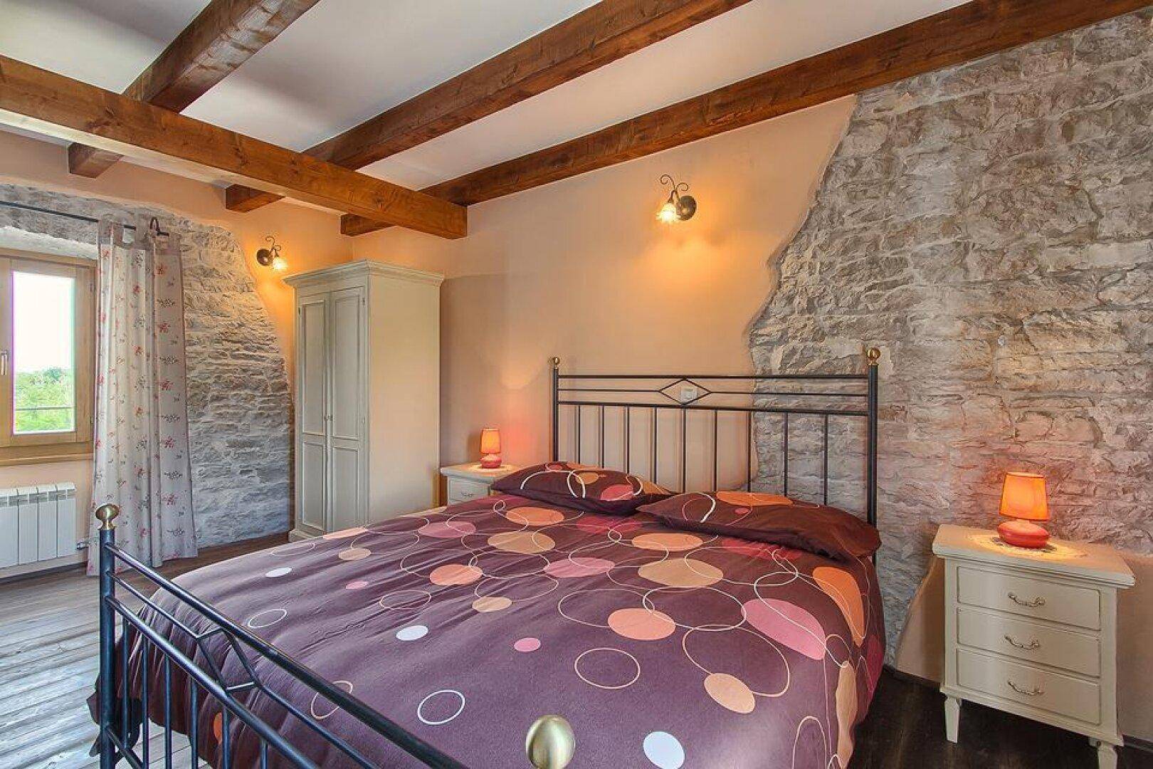 Rustikales Schlafzimmer mit freigelegten Holzbalken, Steinwänden und einem gemütlichen Doppelbett.