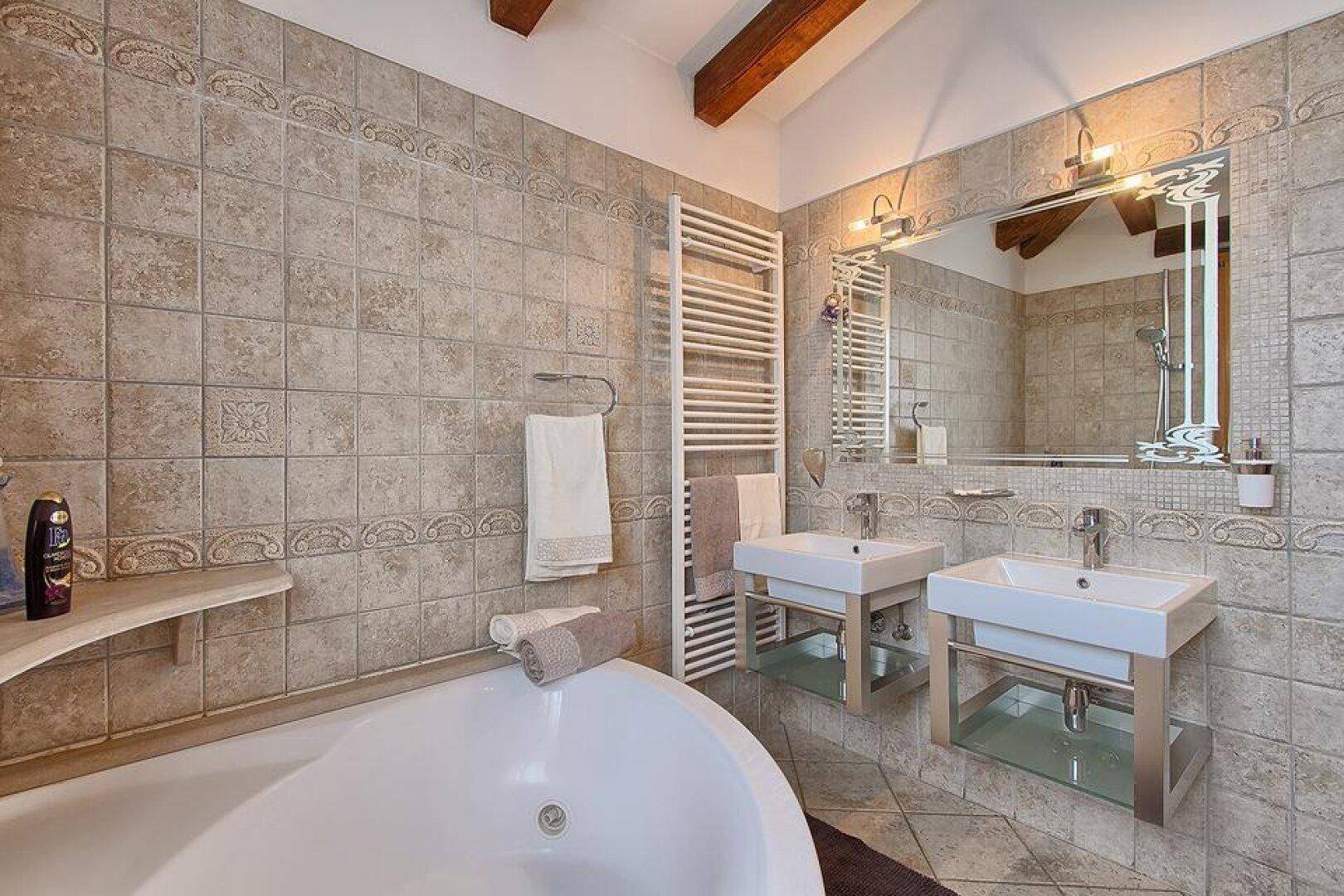 Elegantes Badezimmer mit Eckbadewanne, Doppelwaschbecken, großem Spiegel und beheiztem Handtuchhalter.