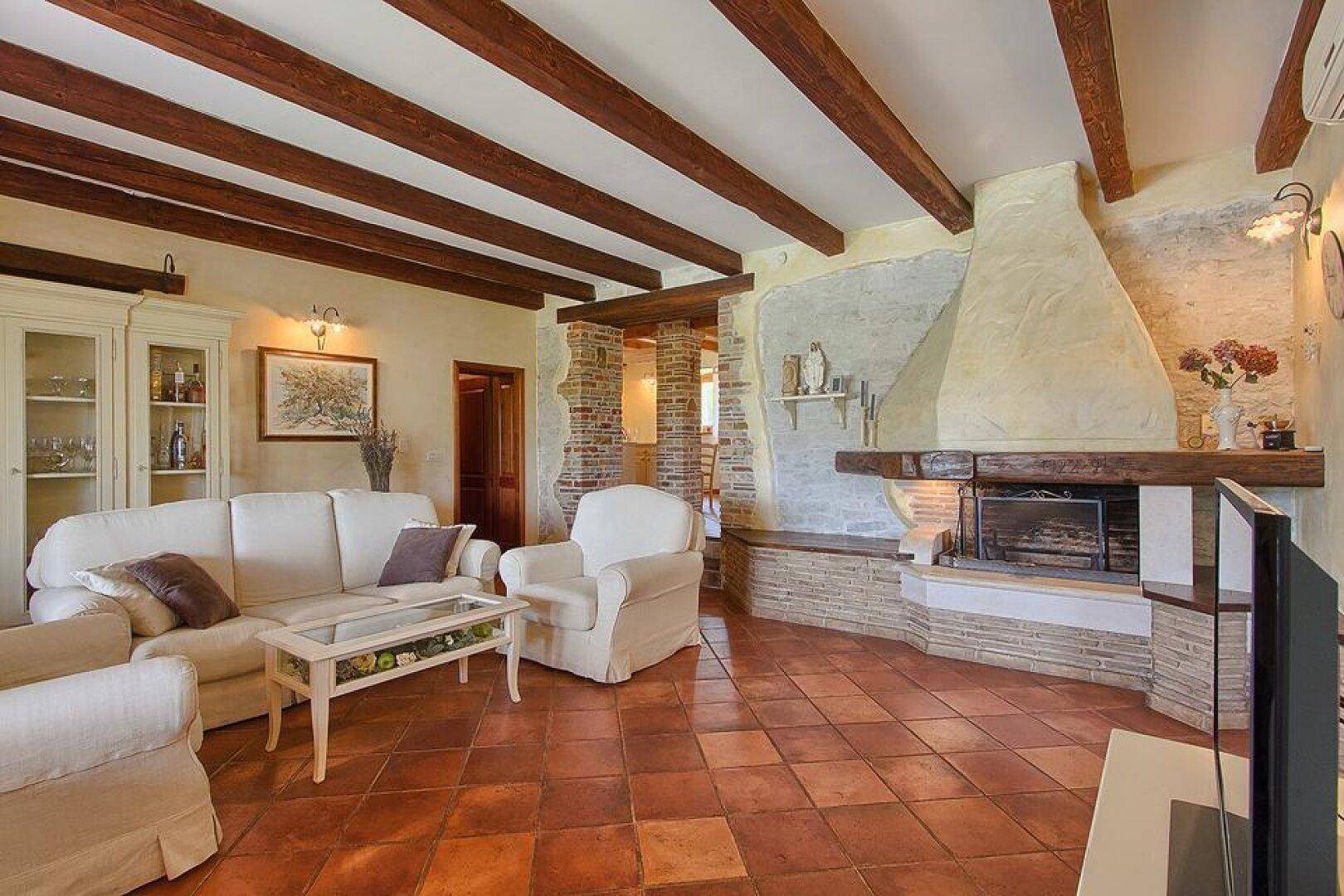 Gemütliches Wohnzimmer mit Terrakottafliesen, freigelegten Holzbalken und einem großen Kamin.