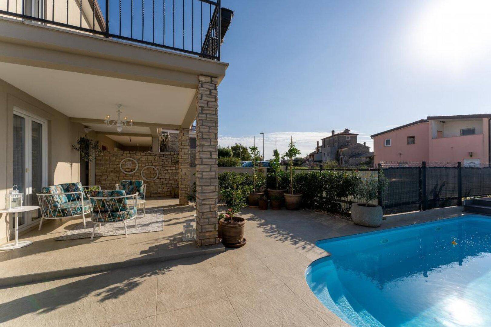 Außenbereich mit großem Pool, angrenzender überdachter Terrasse und mediterraner Bepflanzung.