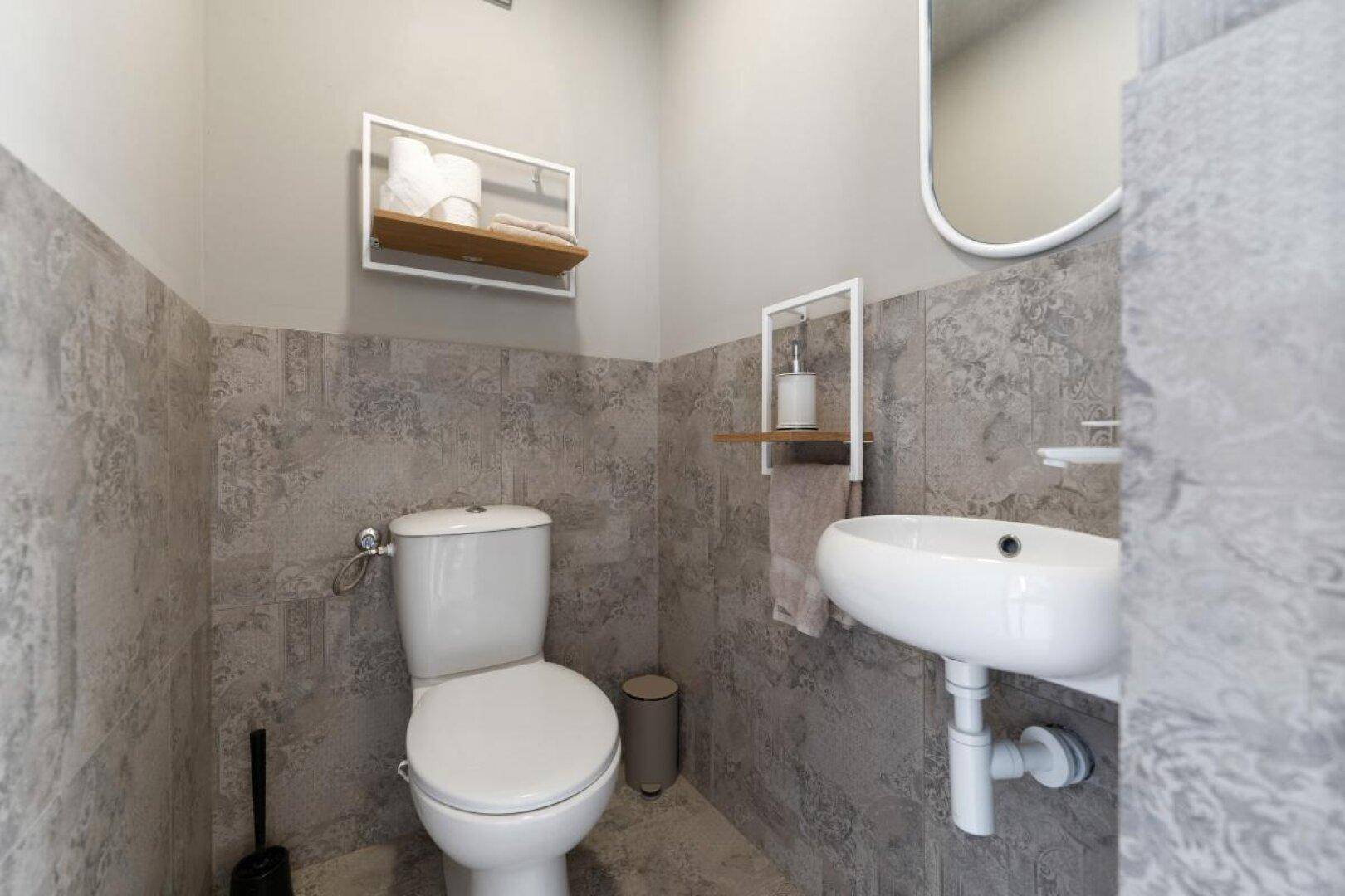 Modernes Gäste-WC mit grauen Fliesen, wandmontierter Toilette und kleinem Waschbecken.