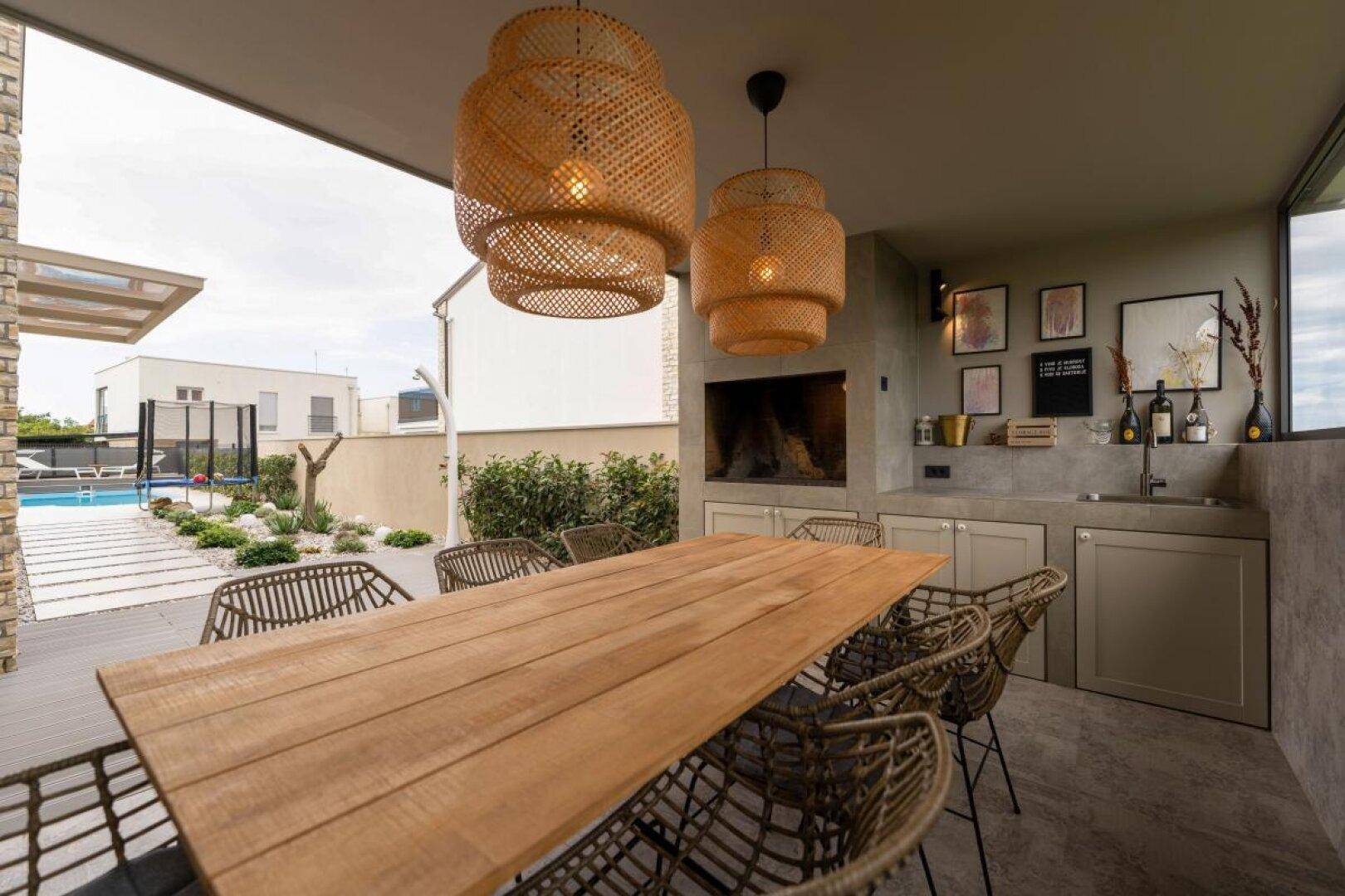 Moderner Essbereich im Freien mit Holztisch, Rattan-Stühlen und Blick auf den Pool.