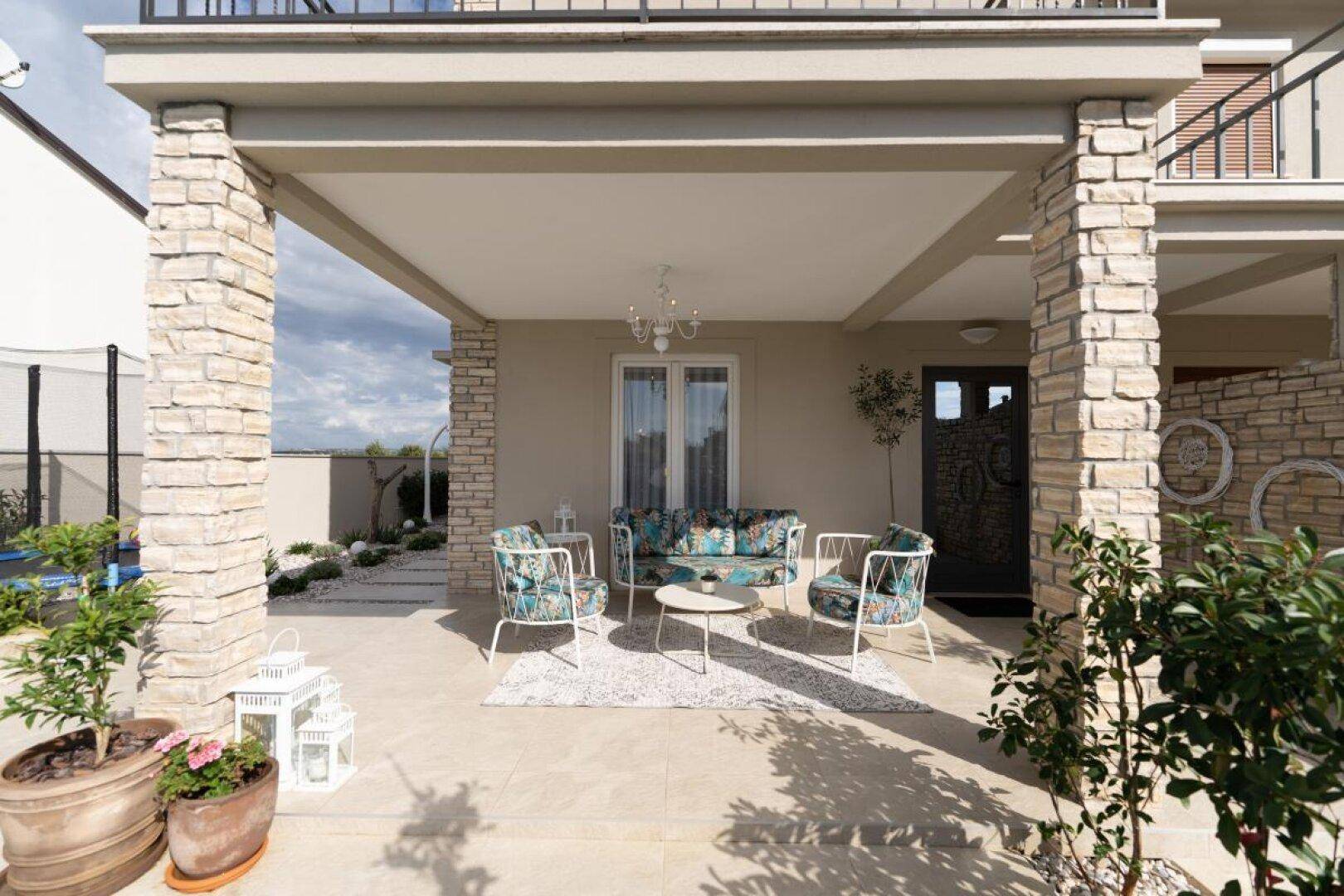 Überdachte Terrasse mit Lounge-Möbeln, Eingangsbereich und dekorativen Topfpflanzen.